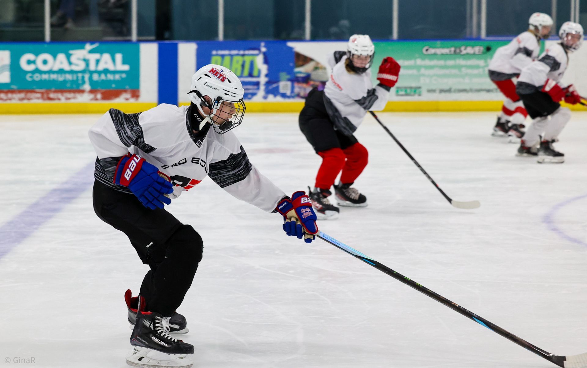 Ice hockey players in white jerseys skating and stickhandling on an indoor rink