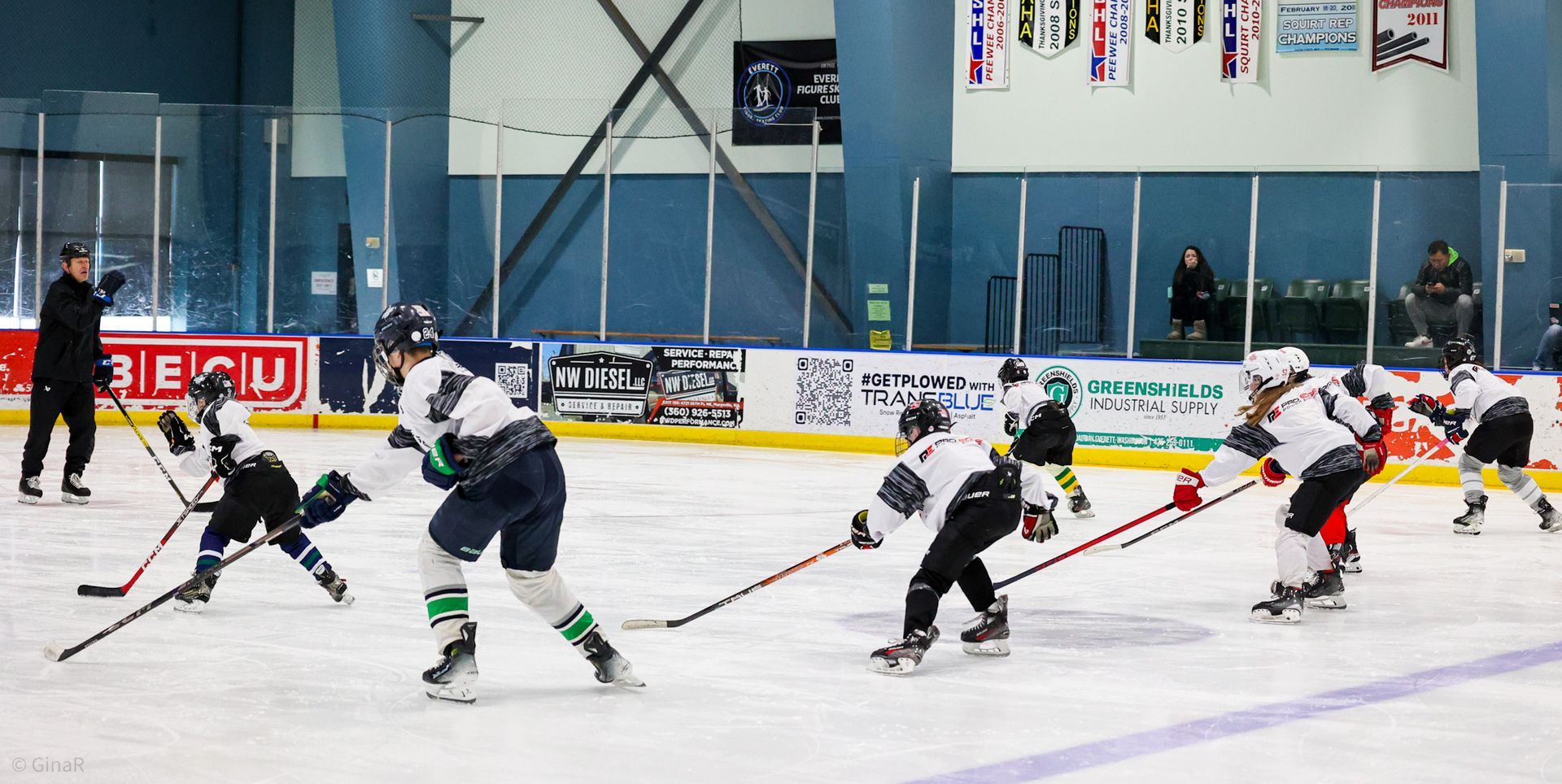 Youth hockey players skating and battling for the puck on an indoor rink.