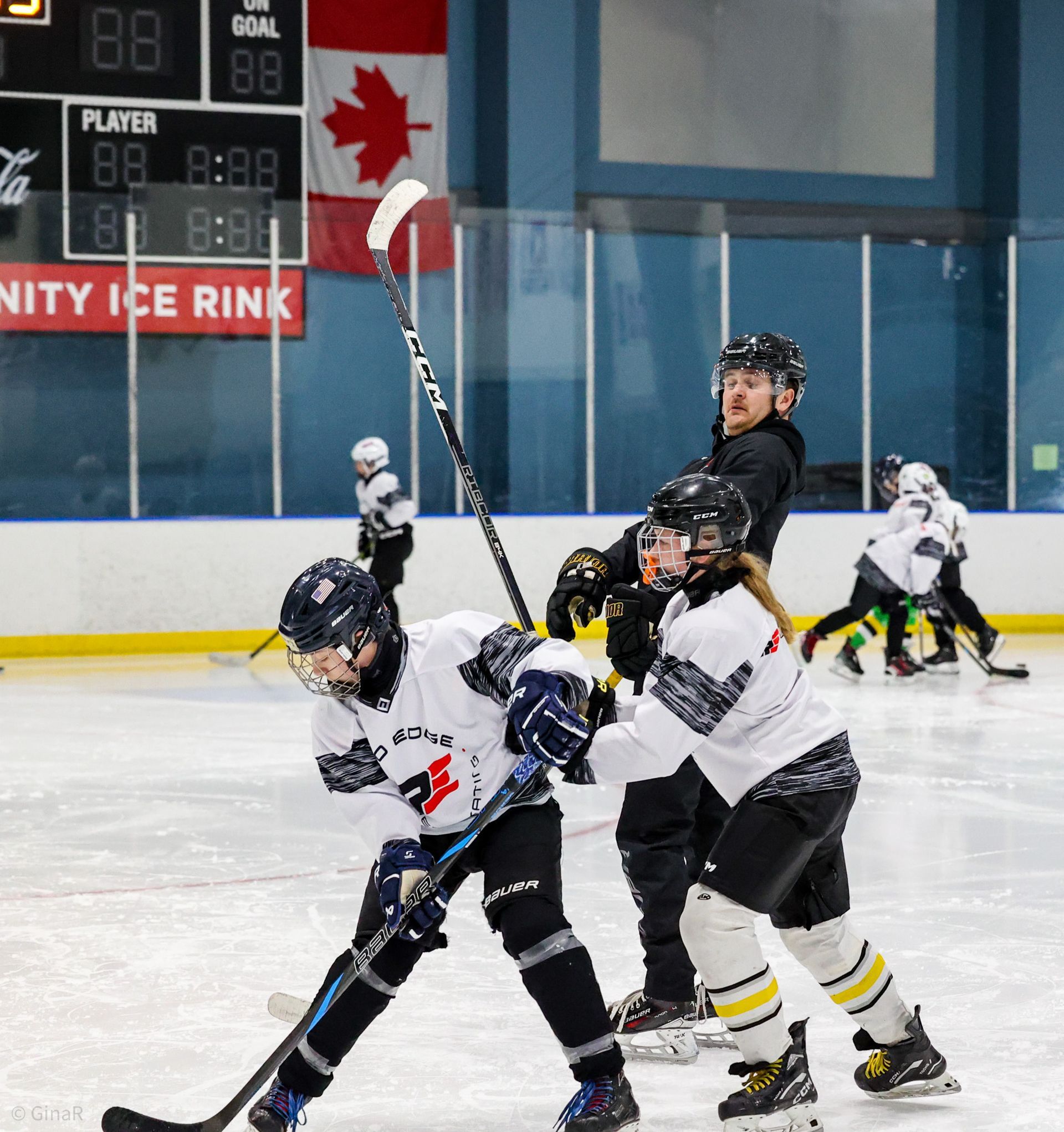 Youth hockey players in black and white jerseys battle for the puck on an indoor ice rink.