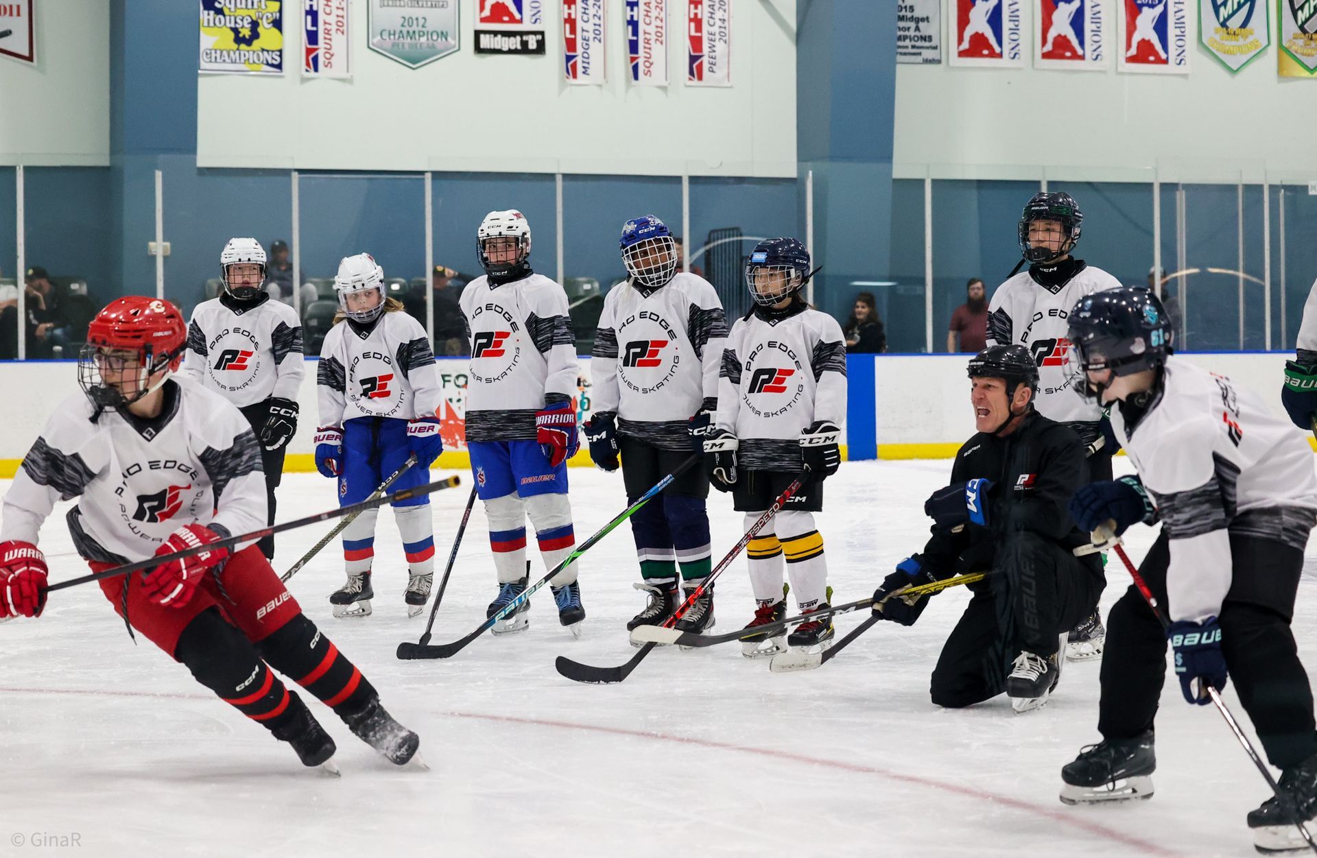 Youth ice hockey players in white and dark jerseys practice on an indoor rink.