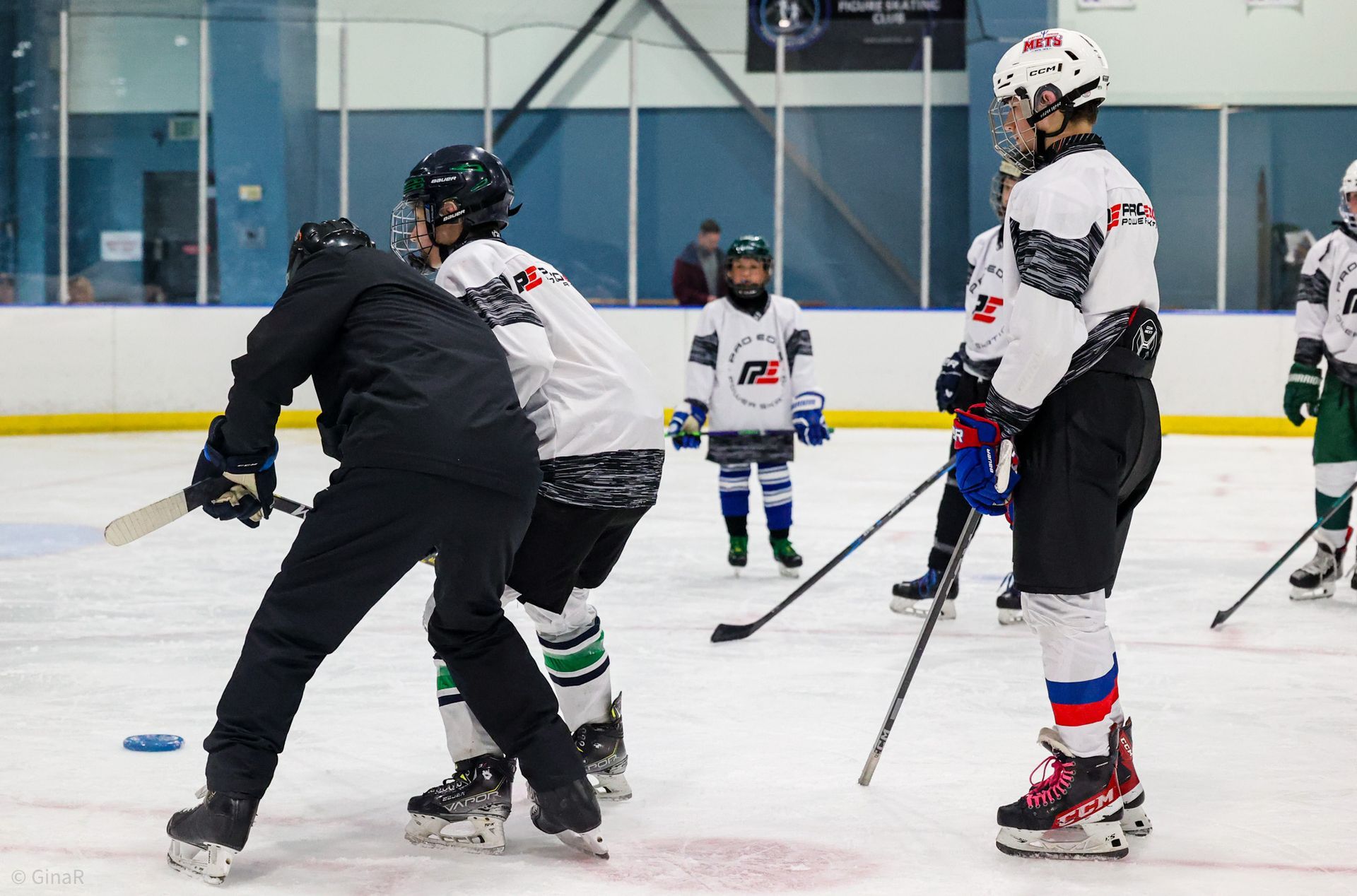Youth hockey players and a coach on an indoor ice rink, practicing with sticks and pucks