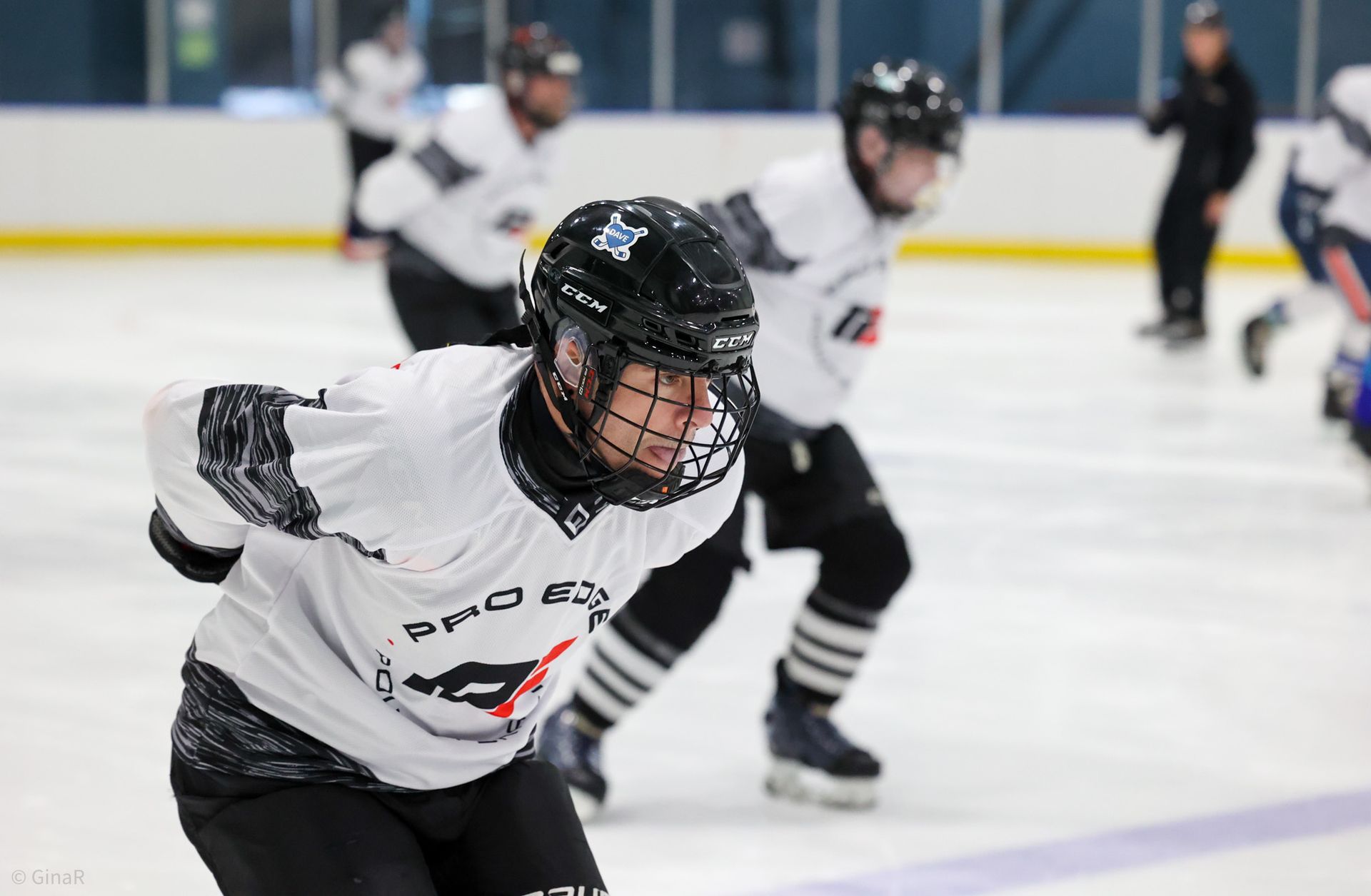 Youth hockey players in white jerseys skate on an indoor ice rink during practice.