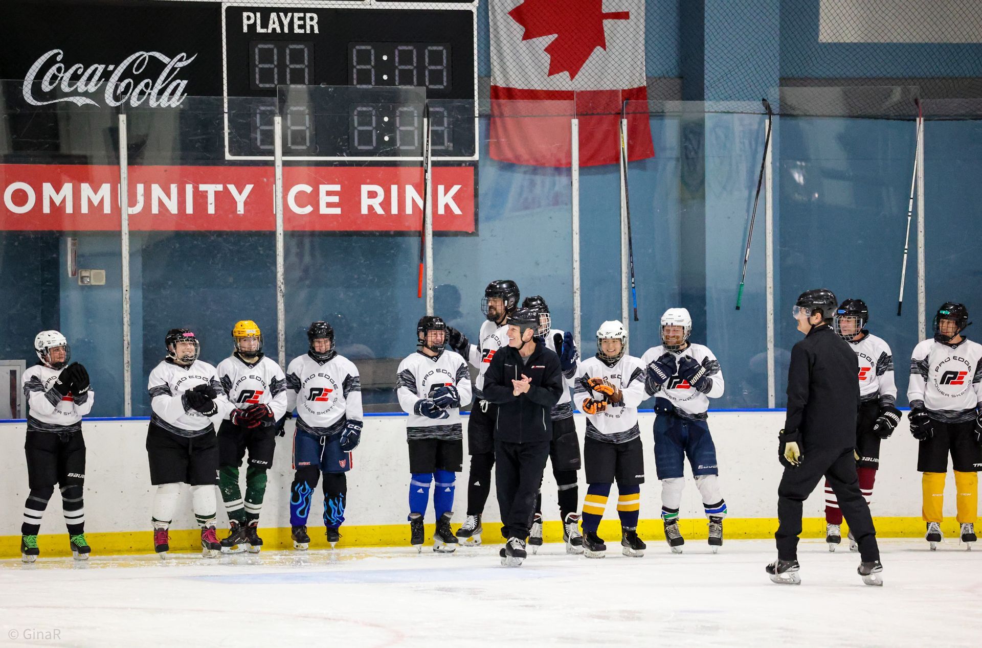 Youth hockey players lined up on the ice at an indoor rink with a Canadian flag in the background