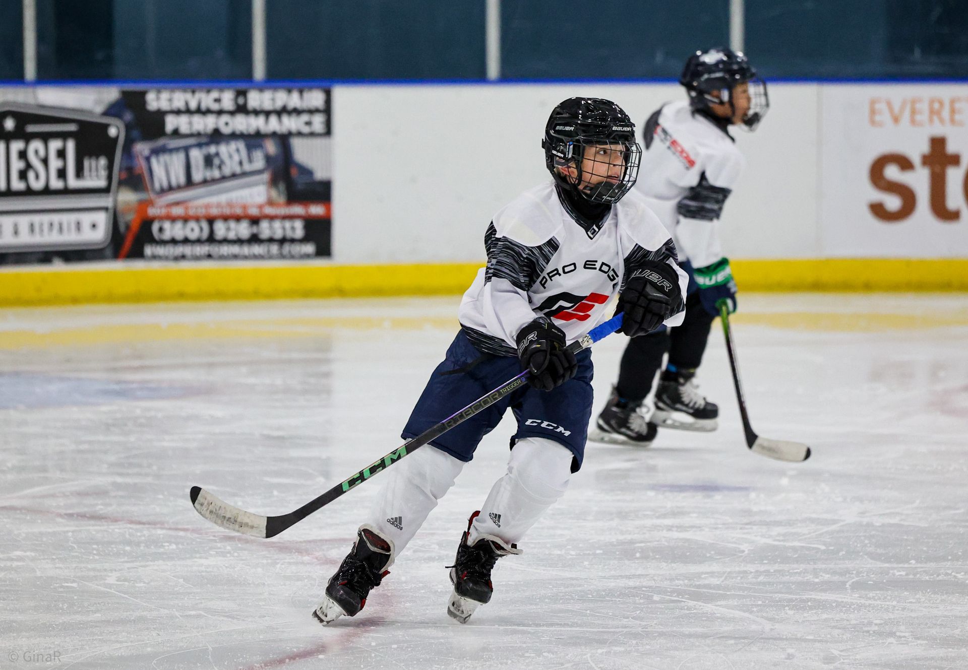 Two hockey players in white and navy skating on ice, one in front handling the puck.