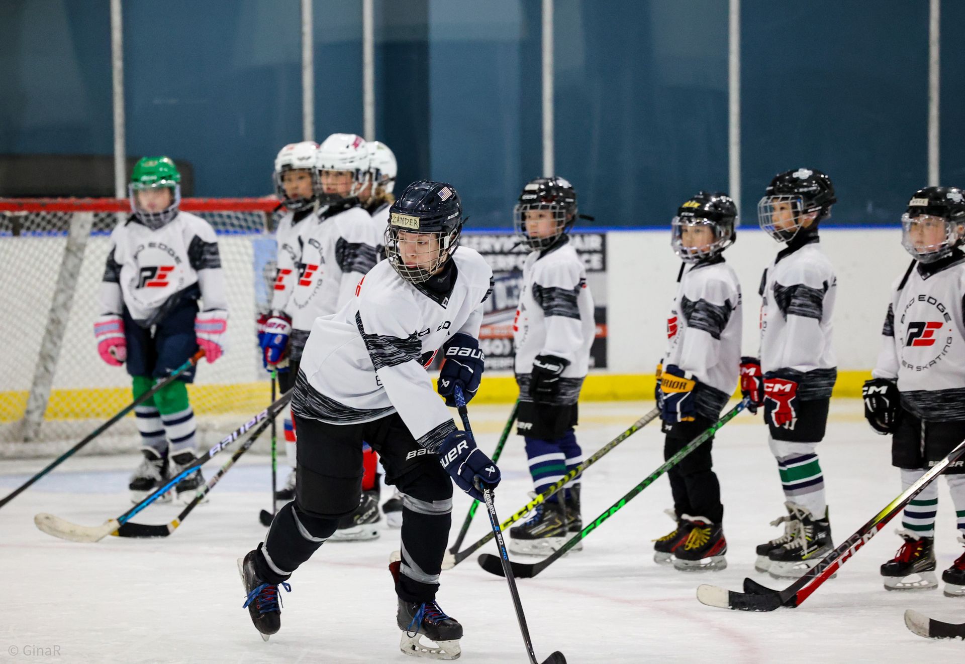 Youth hockey players in white jerseys stand on an indoor rink during practice.