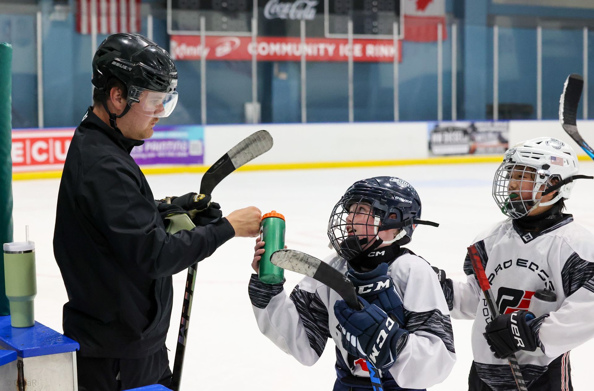 Ice rink coach fist-bumping two youth hockey players on the bench