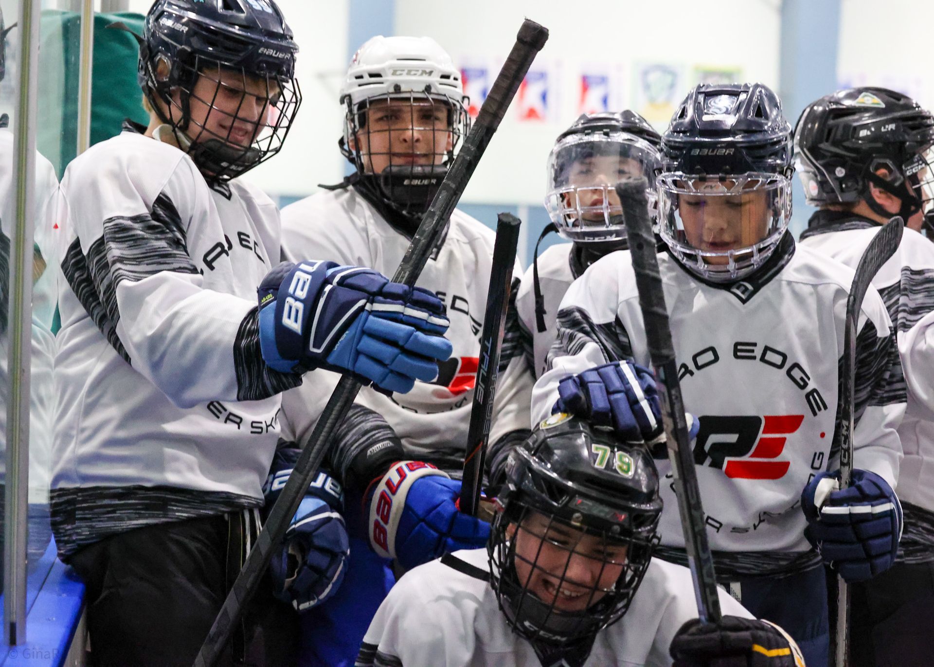 Hockey players in white jerseys huddle tightly, holding sticks on the bench or rink side.