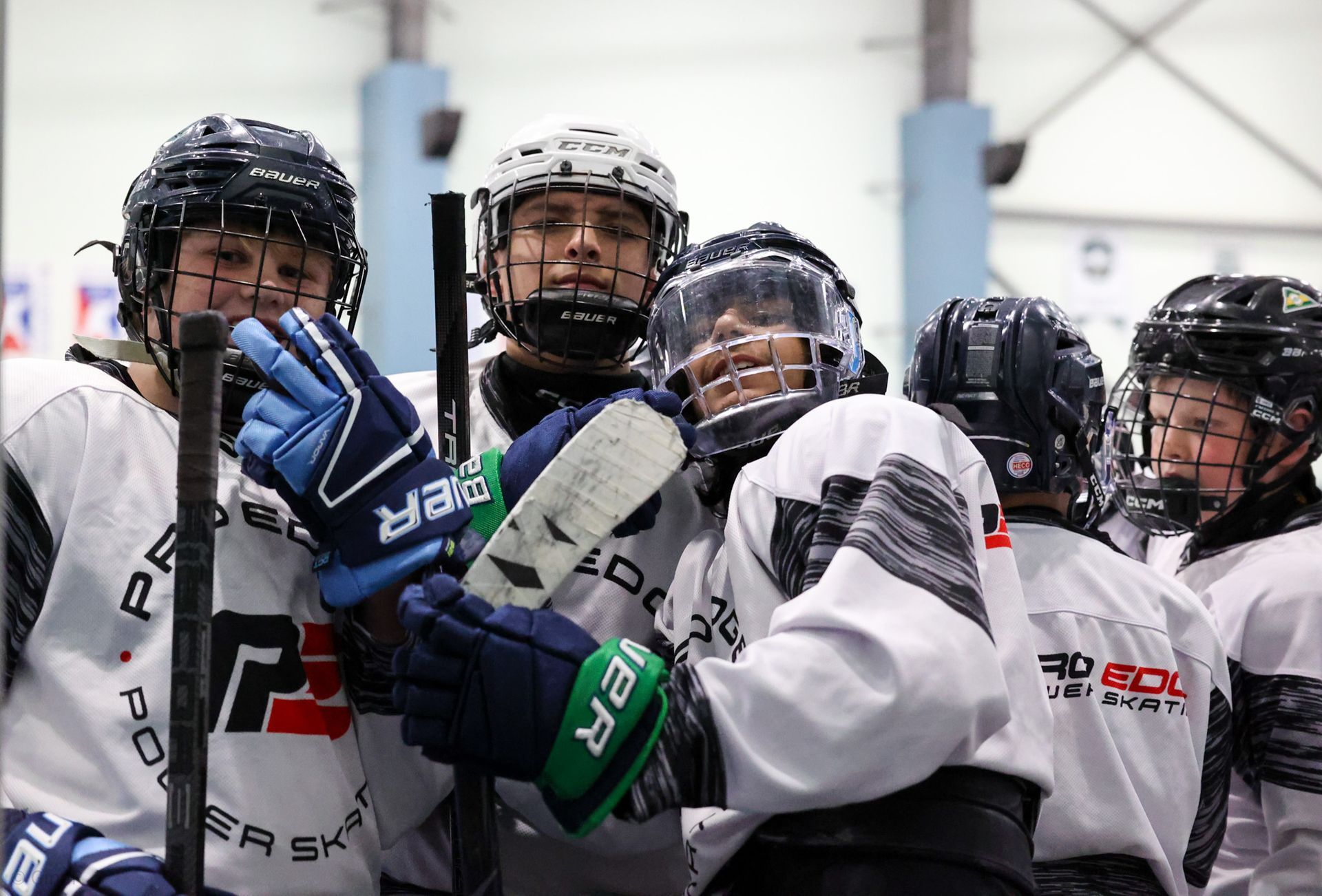 Youth hockey players in white jerseys huddle on the ice, wearing helmets and gloves.