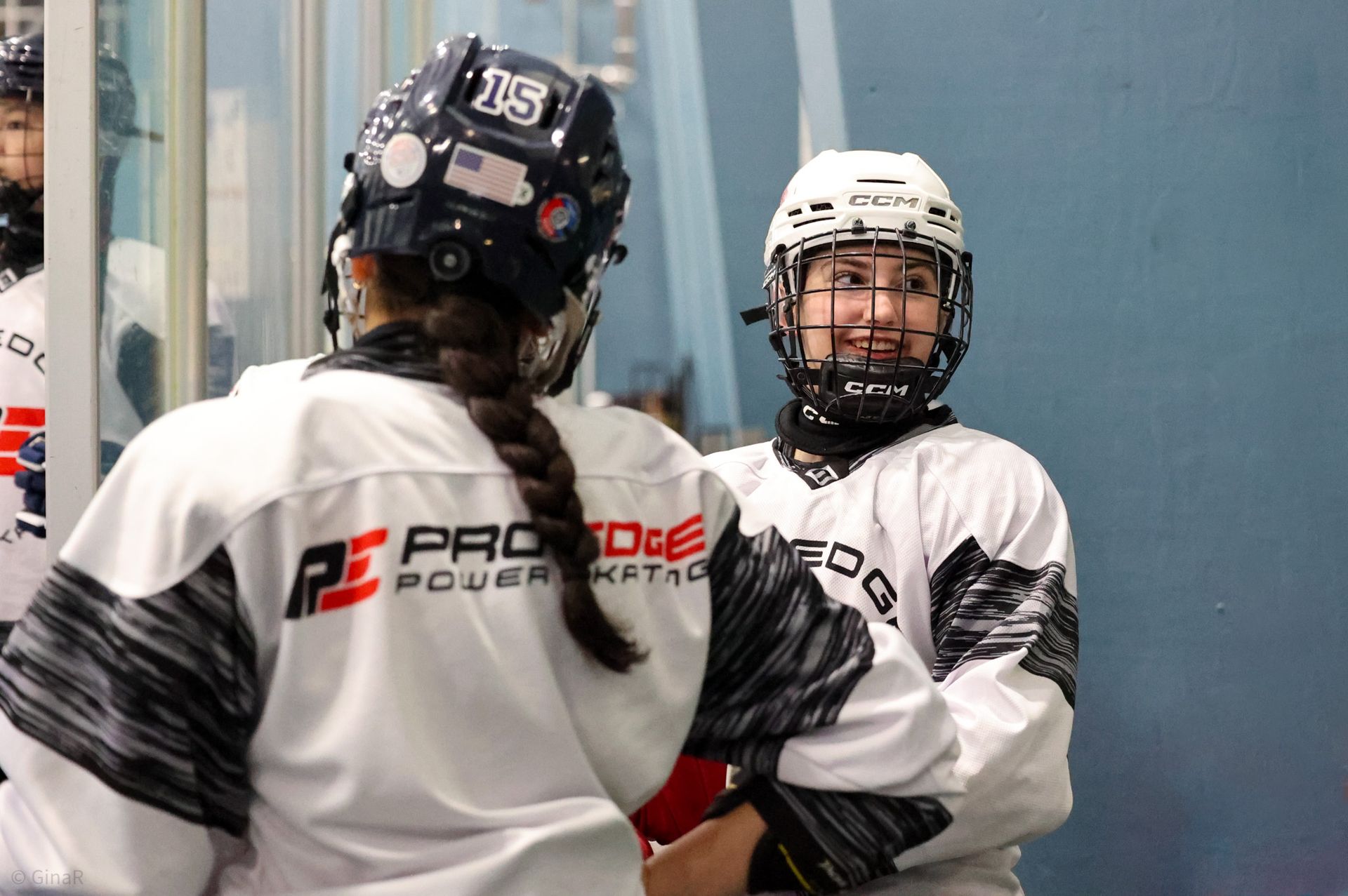 Two hockey players in white jerseys and helmets standing on the ice rink, facing each other near the boards.