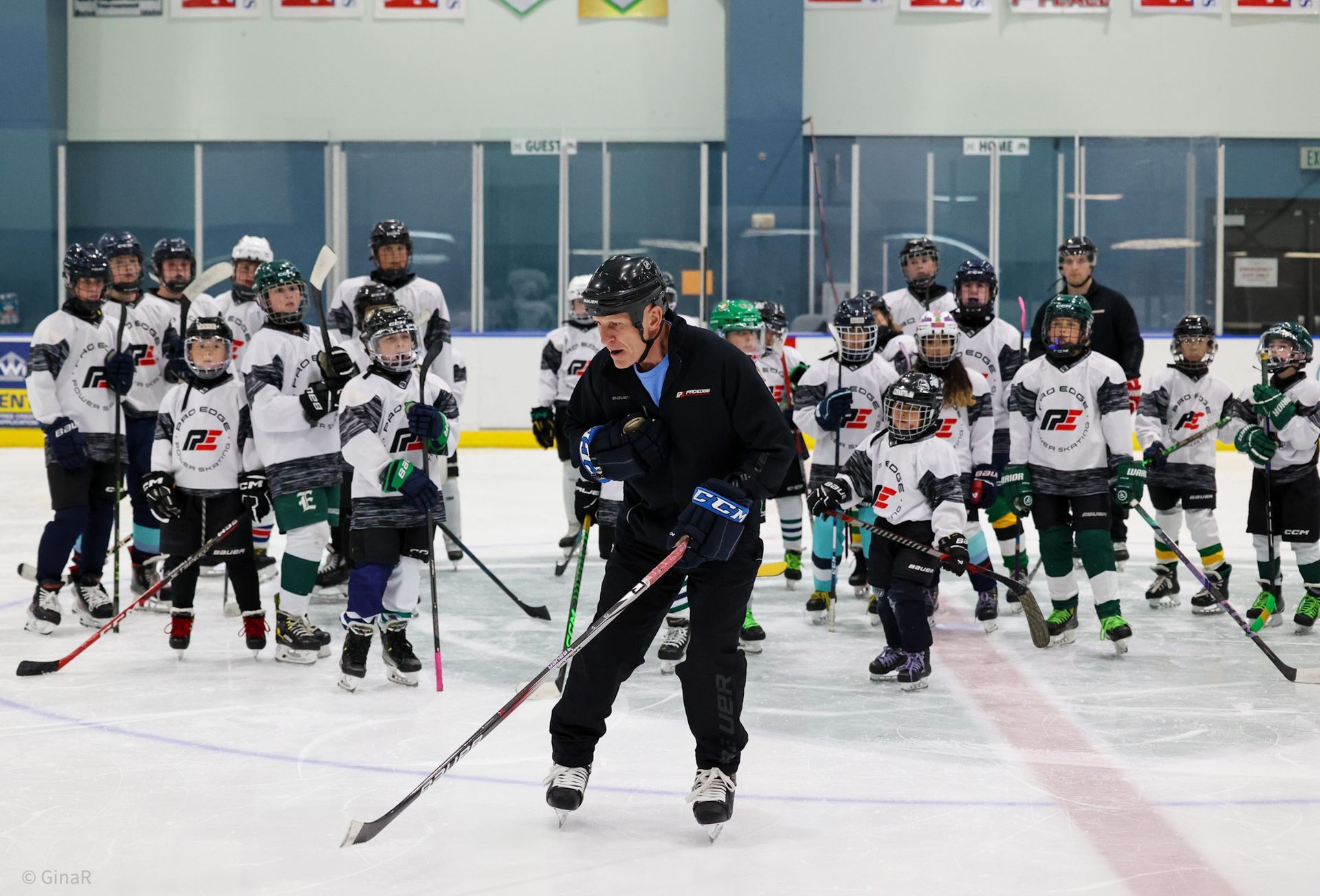 Hockey coach in black leads a group of young players on an indoor rink during practice