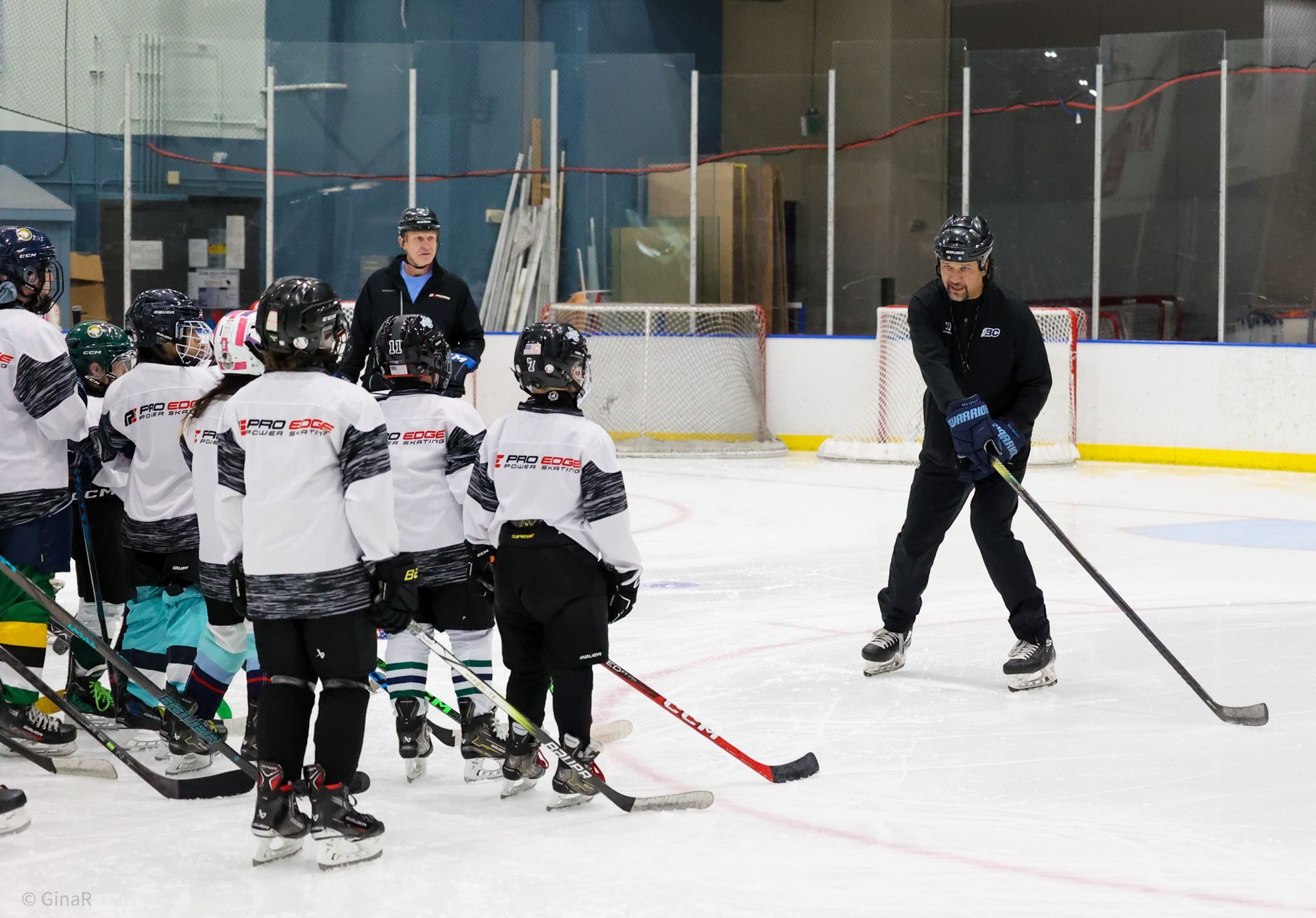 Hockey coach on ice instructing a group of young players in white jerseys at an indoor rink