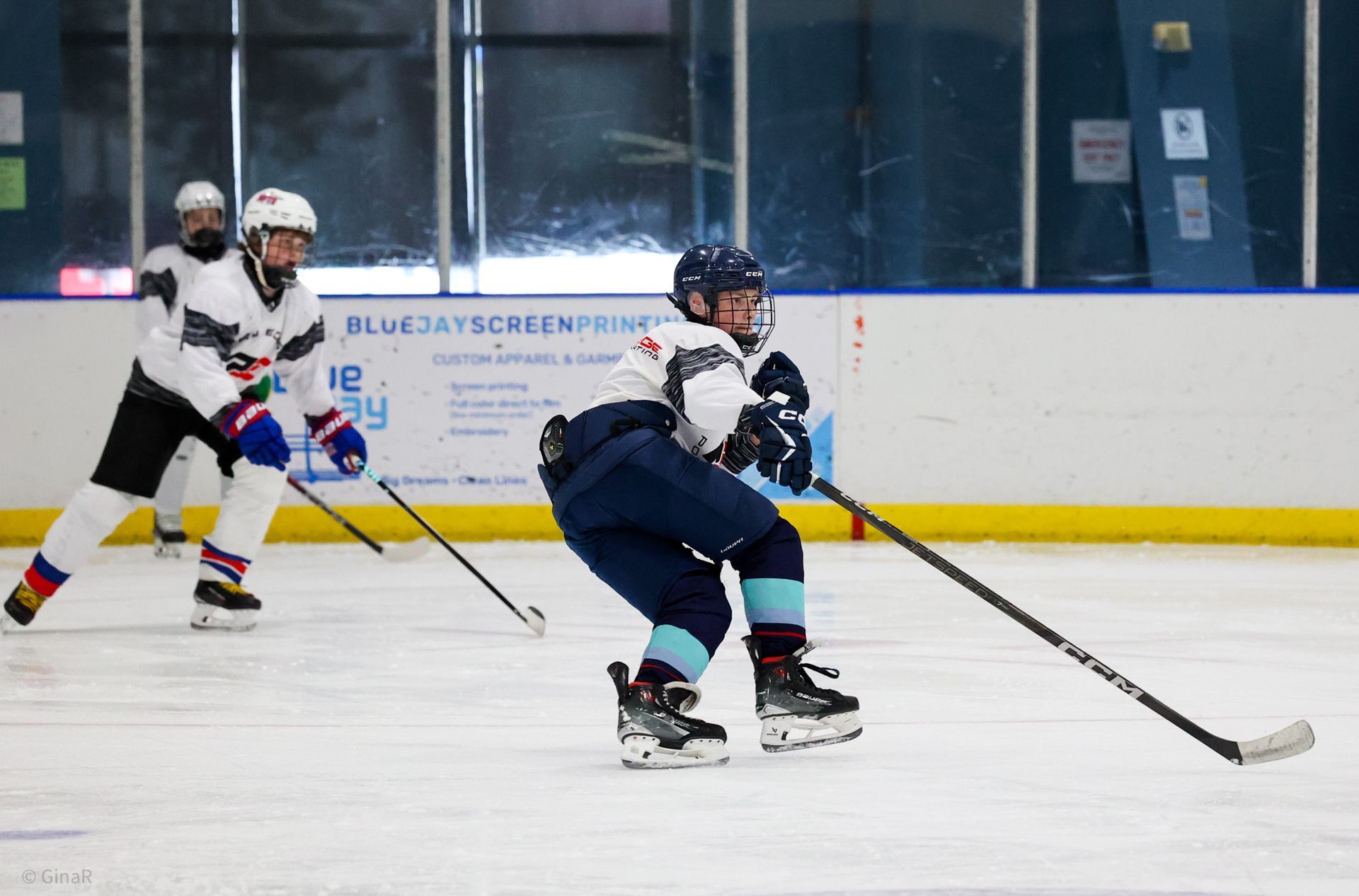 Ice hockey players skating on an indoor rink, one in blue in the foreground with puck