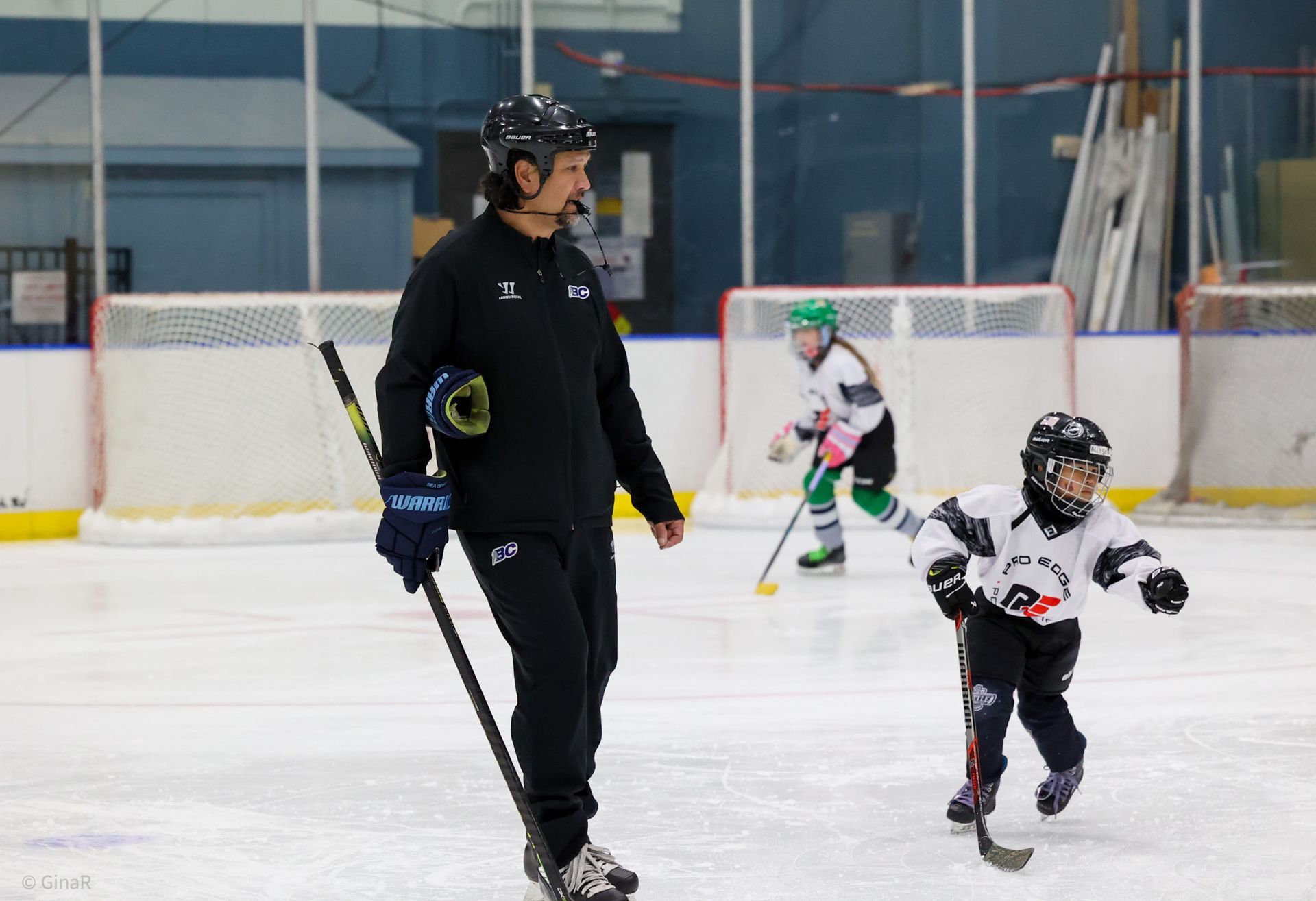 Ice rink scene with a coach and two child skaters practicing on the ice