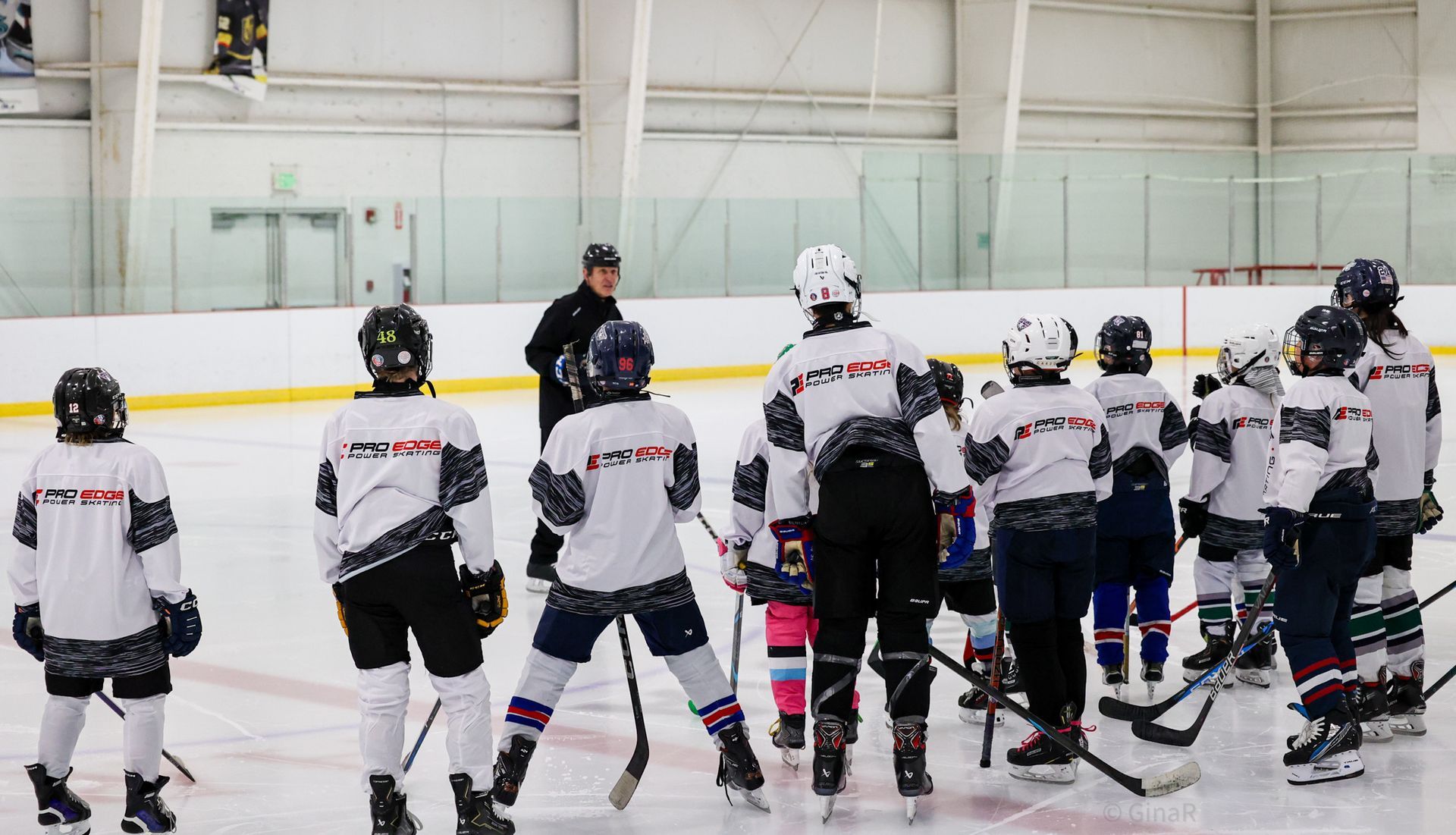 Youth hockey team in white jerseys listening to a coach on an indoor ice rink