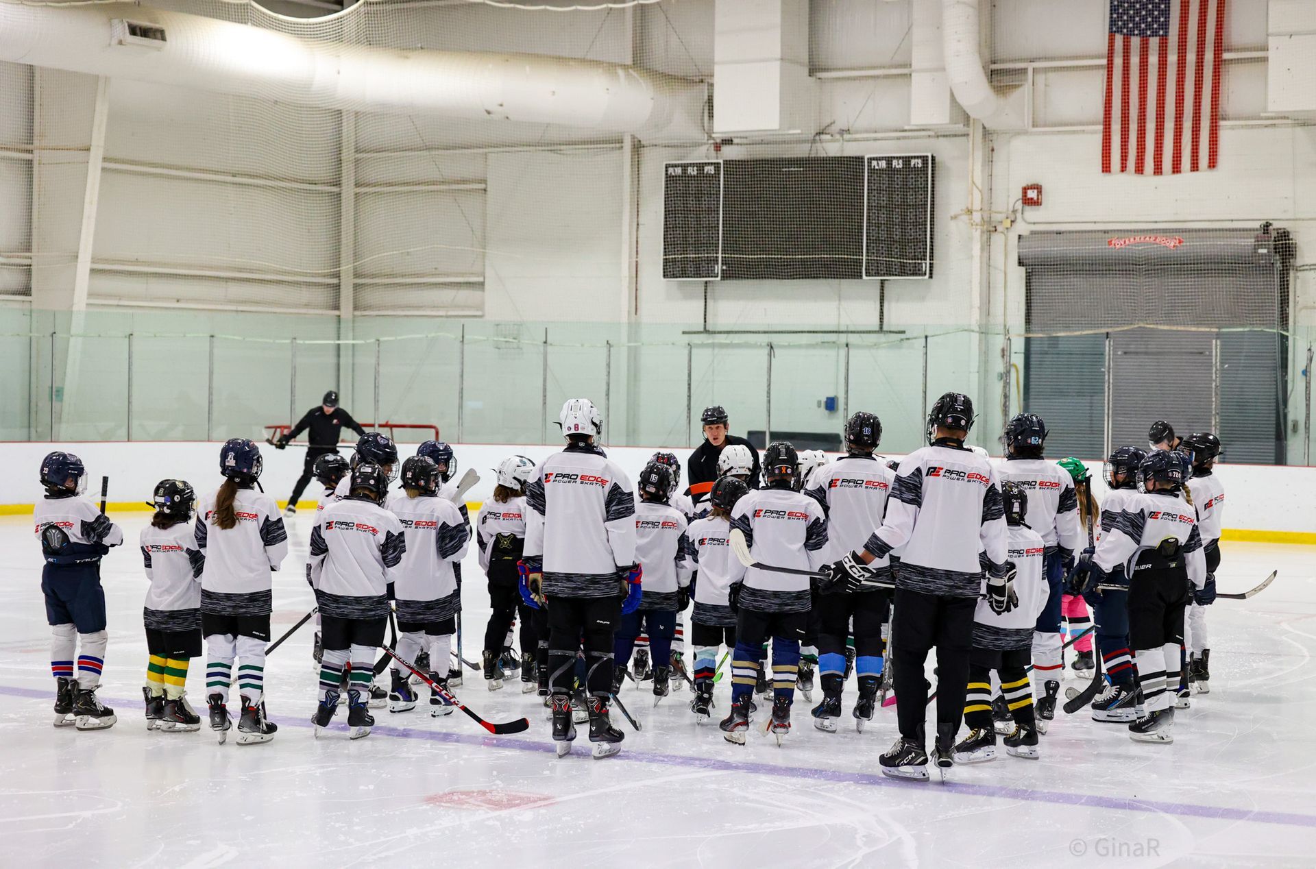 Youth hockey team gathered on the ice in a rink, wearing white jerseys and helmets.