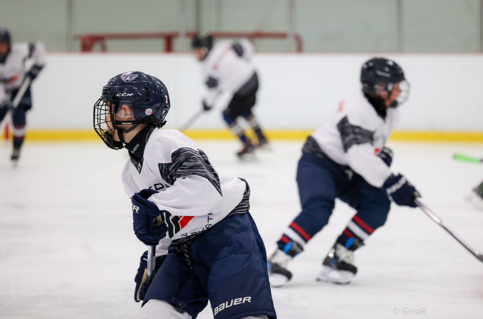 Youth hockey players in white and navy uniforms skating on an indoor ice rink