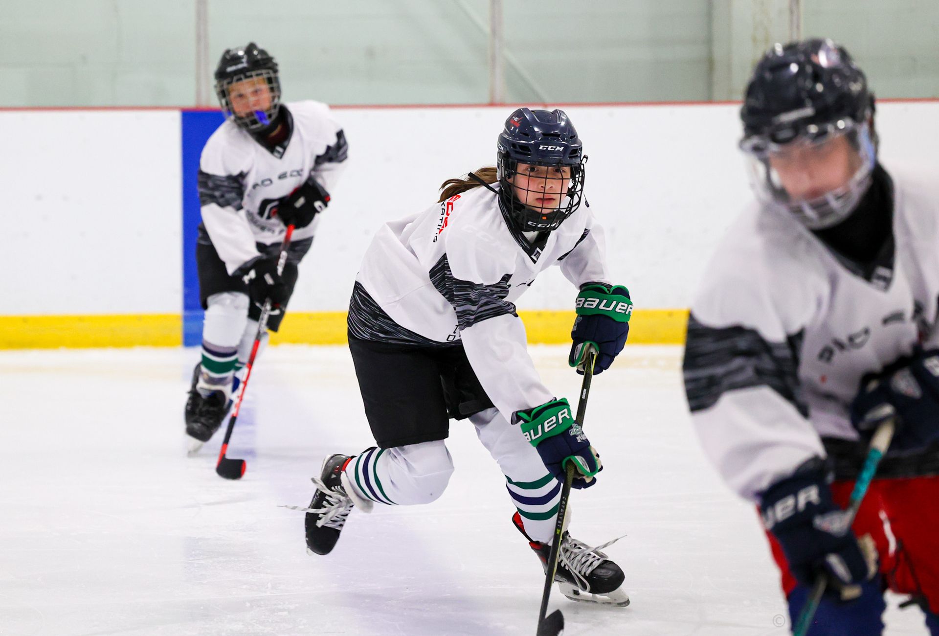 Youth hockey players in white jerseys skating on an indoor ice rink during a game