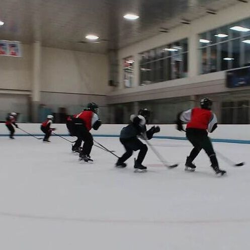 Hockey players in red and black jerseys skating indoors on an ice rink during practice