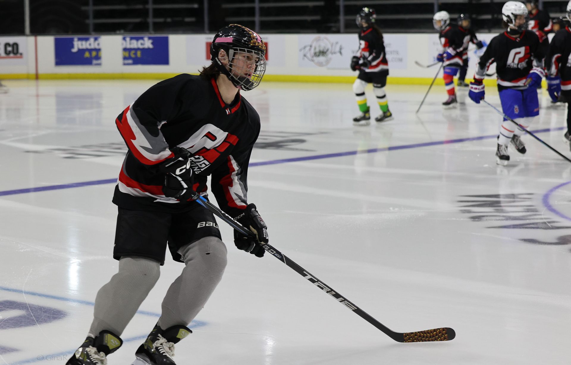 Hockey player in black and red skates with puck on indoor ice rink during a game