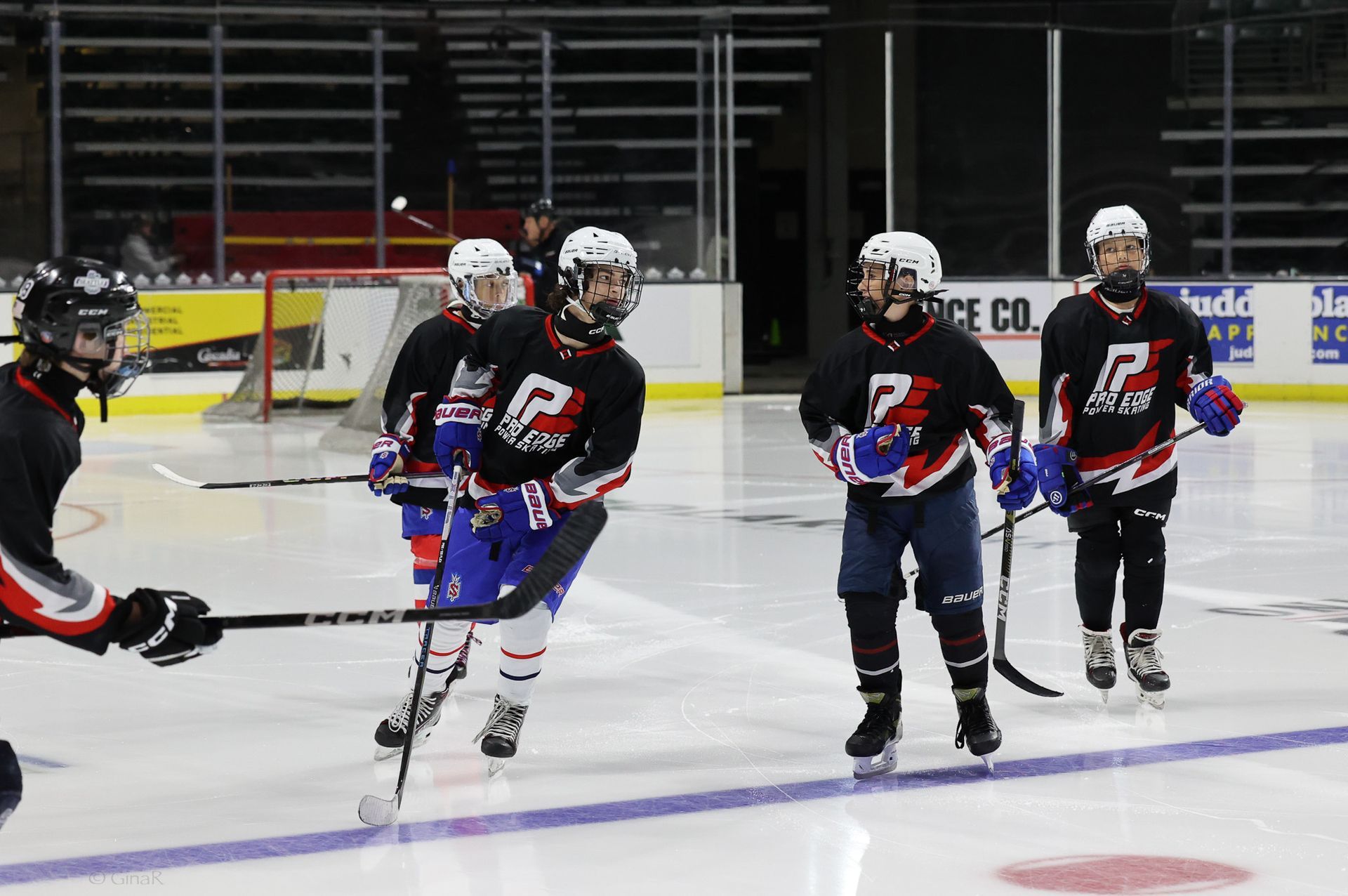 Hockey players in black jerseys skate on an indoor ice rink during practice.