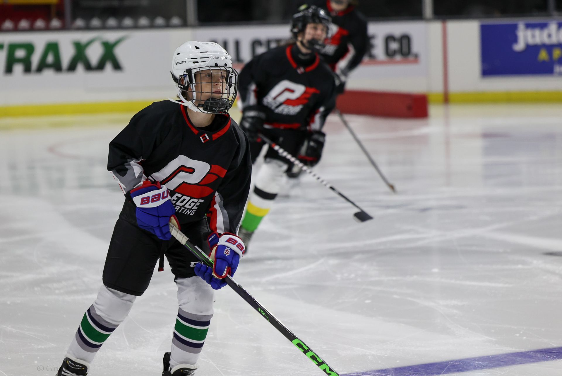 Ice hockey players in black jerseys skating on the rink, one in the foreground handling the puck.