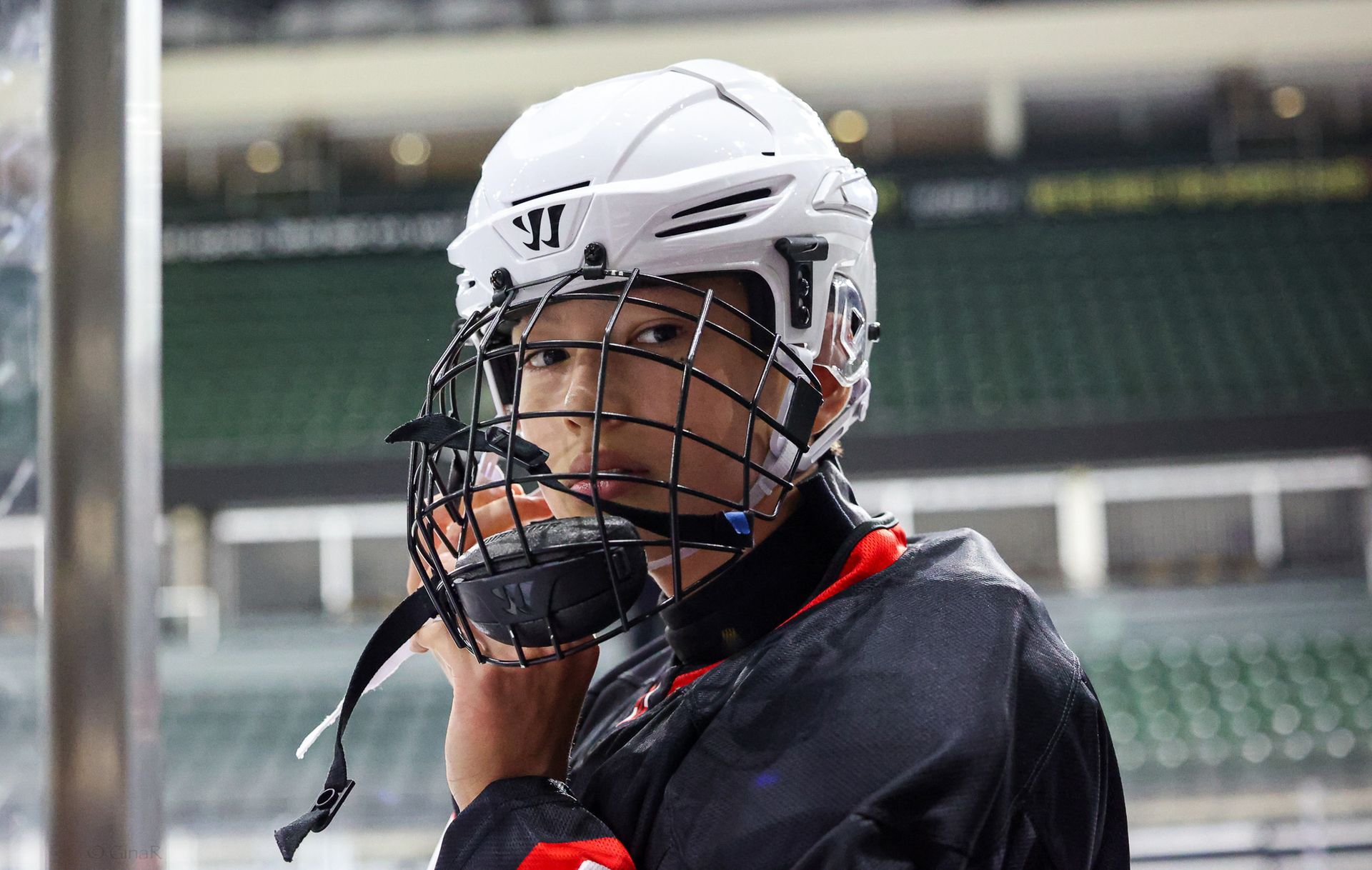 Ice hockey player in white helmet and black jersey adjusting a face cage on the rink