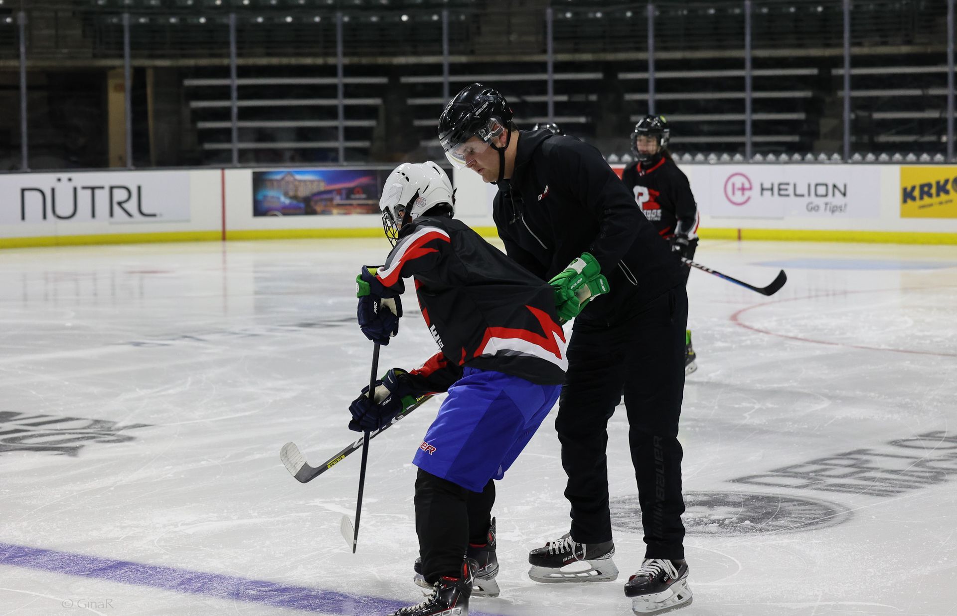 Hockey players in black and red gear face off on an indoor ice rink.