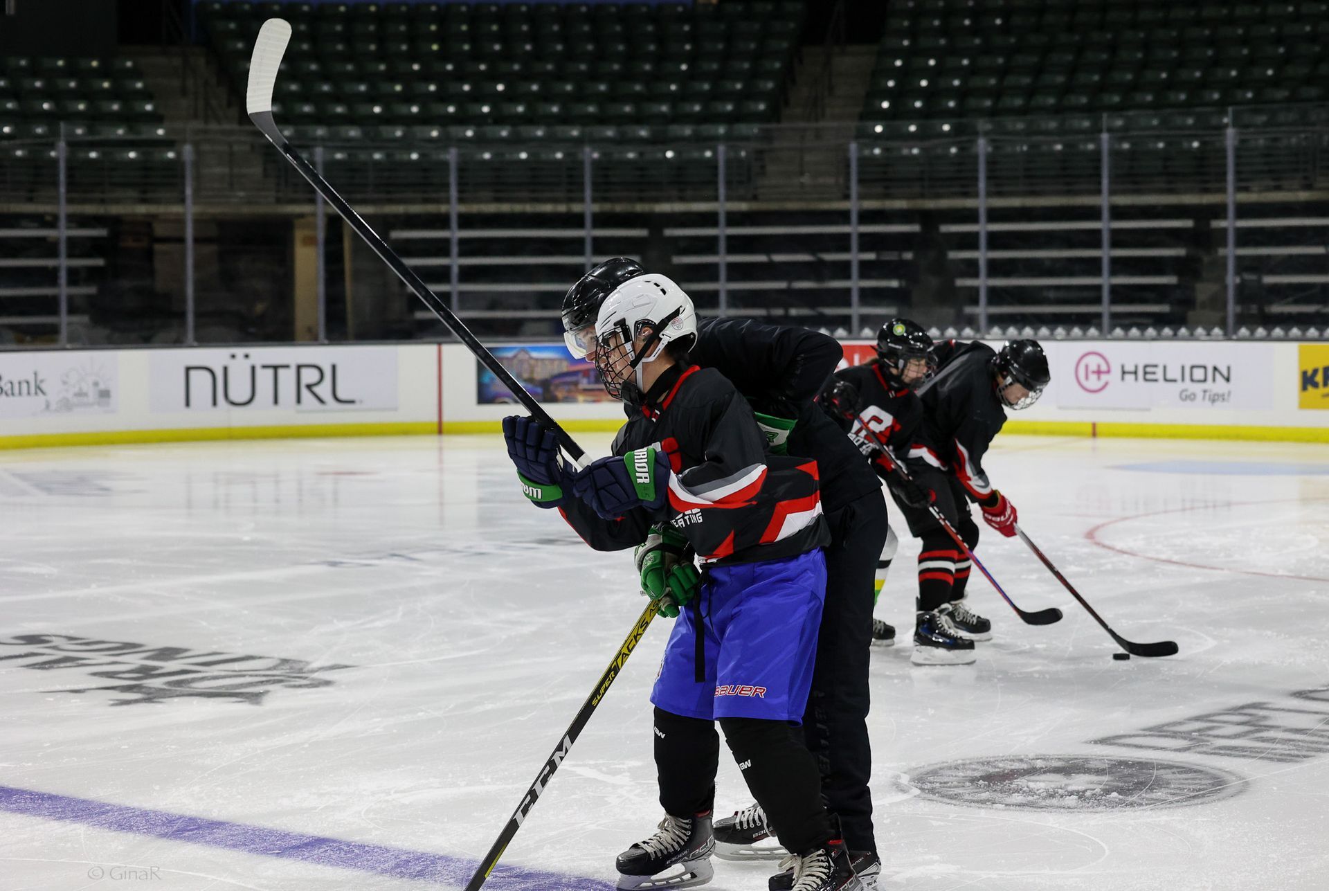 Ice hockey players in black jerseys warm up on an indoor rink, one in a white helmet holding a stick.