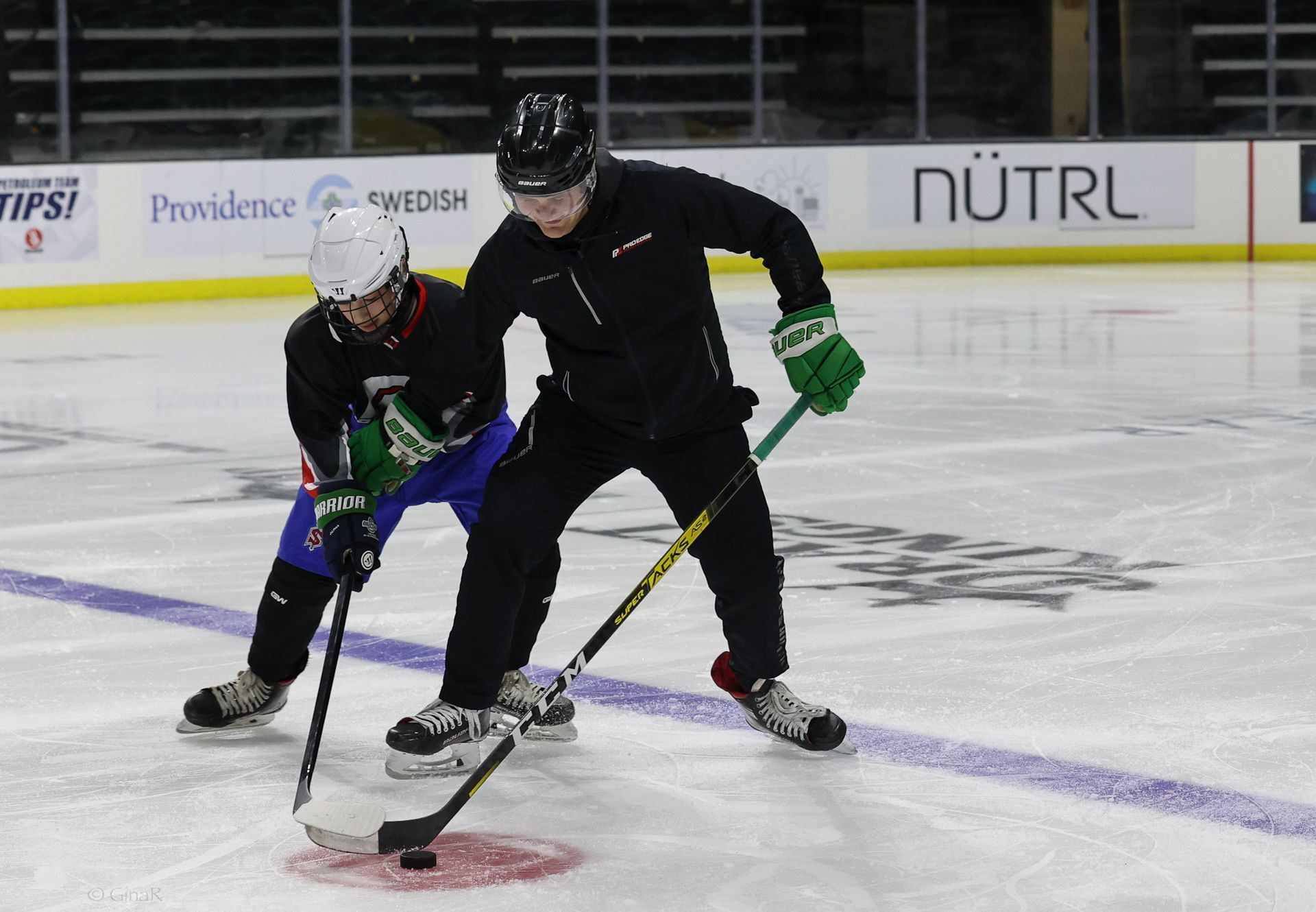 Two hockey players in black uniforms battle for the puck on an ice rink.
