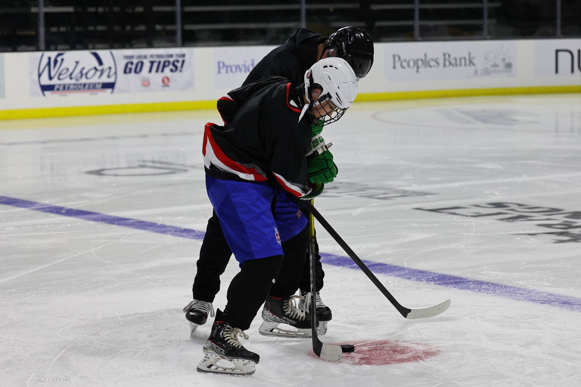 Two hockey players in black and green jerseys grapple on an ice rink during a game.
