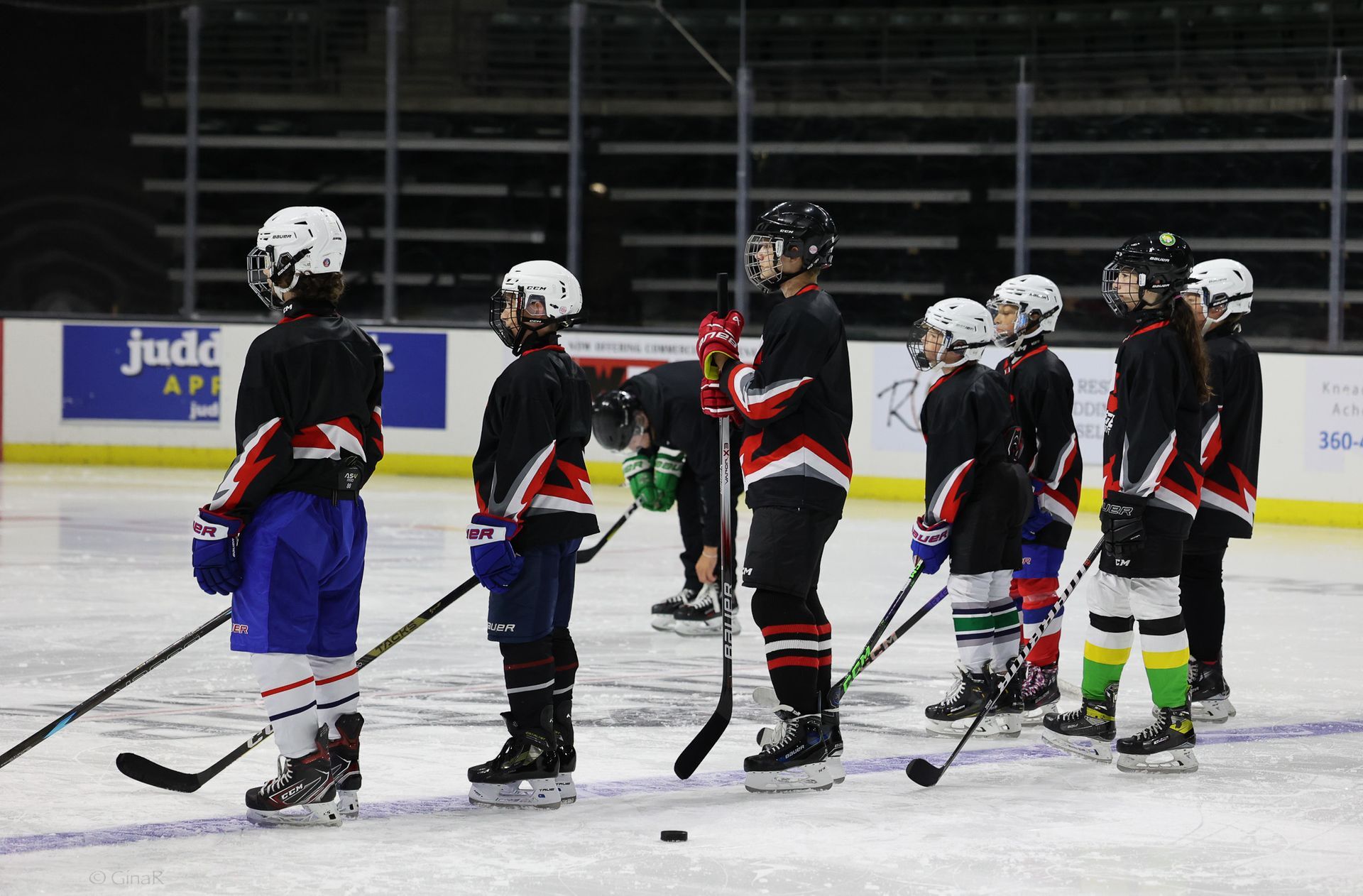 Youth hockey players in black jerseys and colorful socks standing on an ice rink with sticks raised