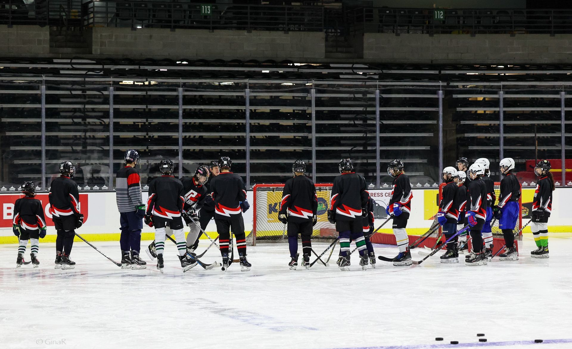 Hockey players in black and red gather on the ice near the boards during a game break.
