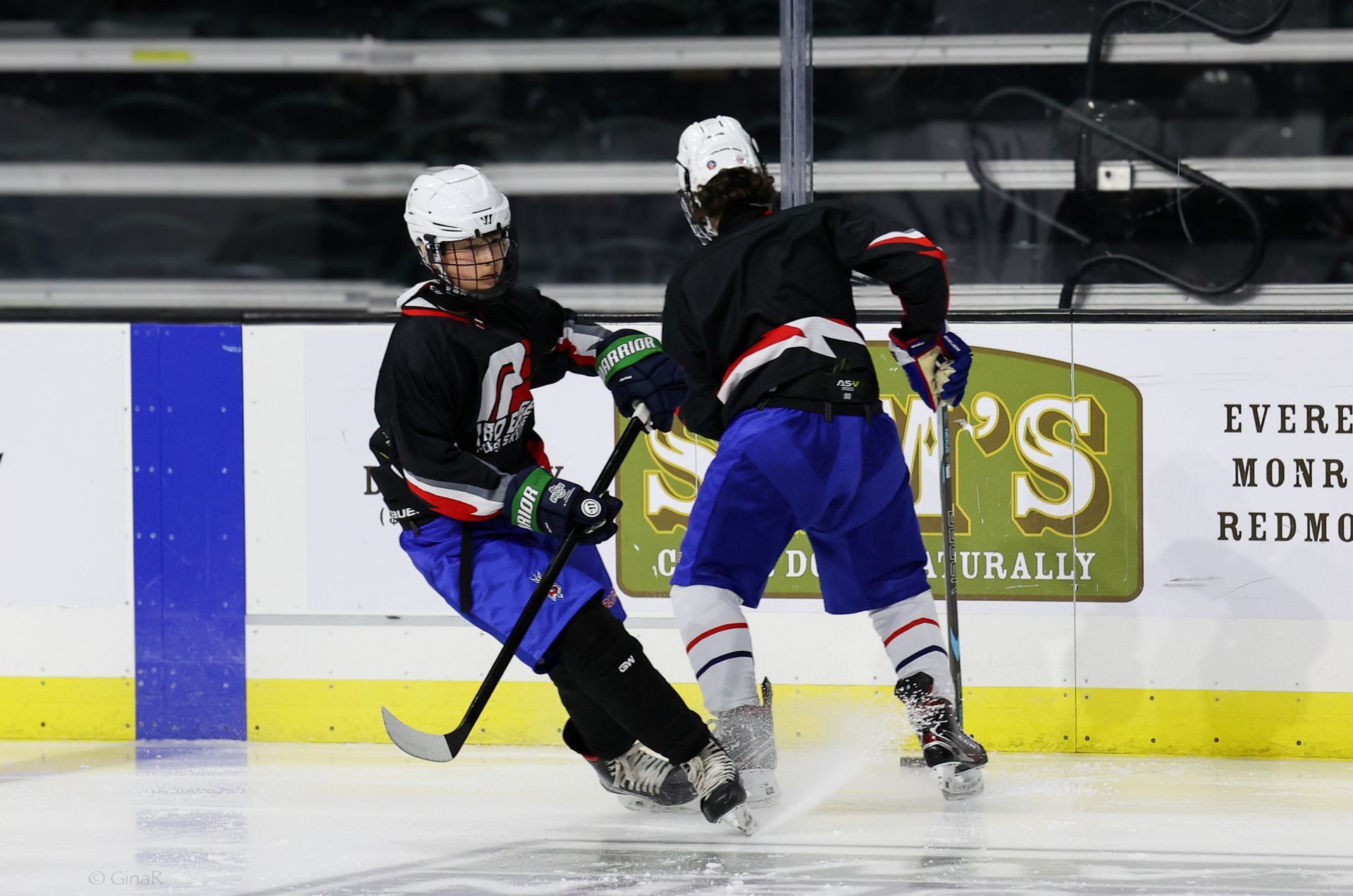Two hockey players in black jerseys battle for the puck on an indoor ice rink