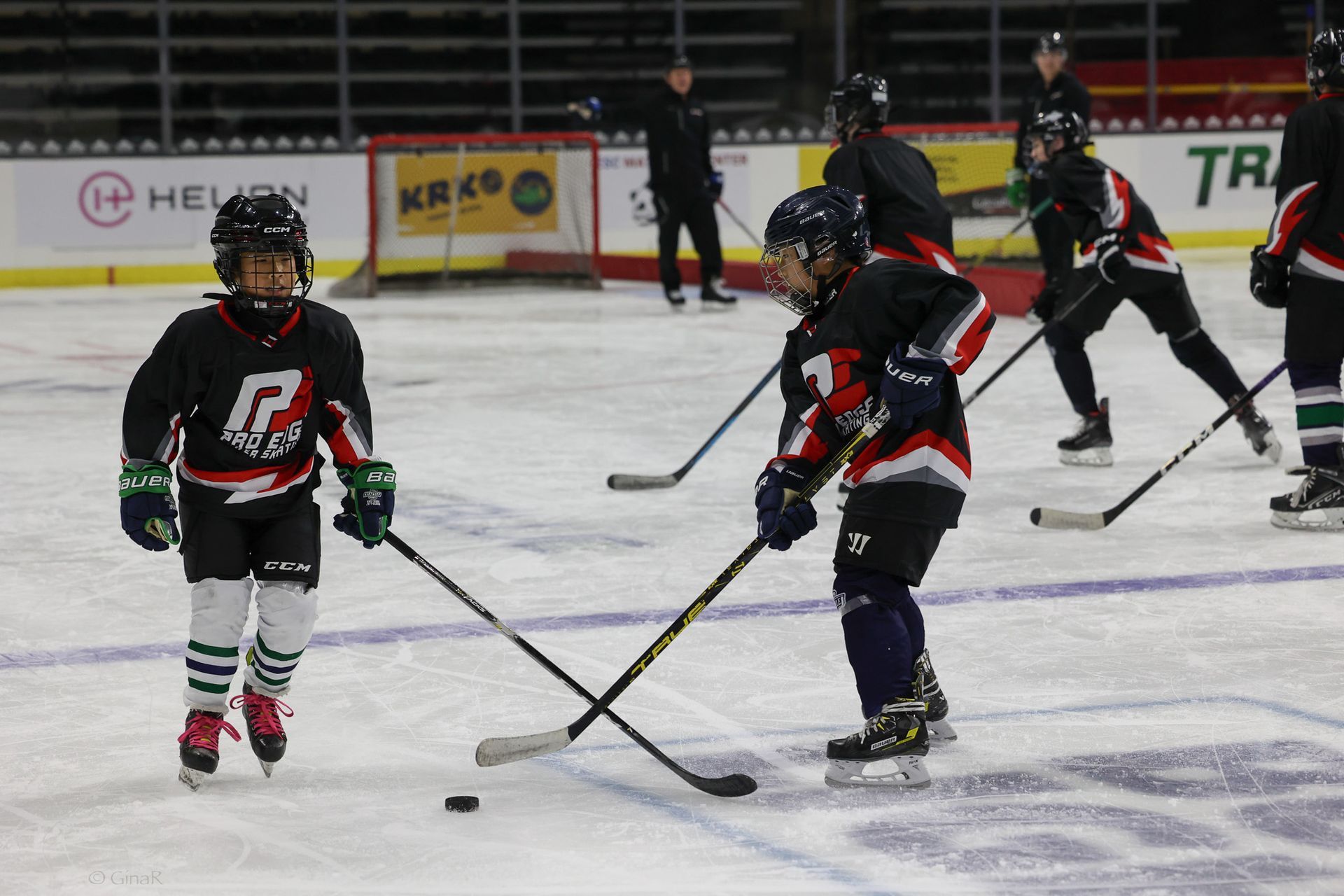 Youth hockey players practicing on an indoor ice rink, with pucks and sticks in motion.