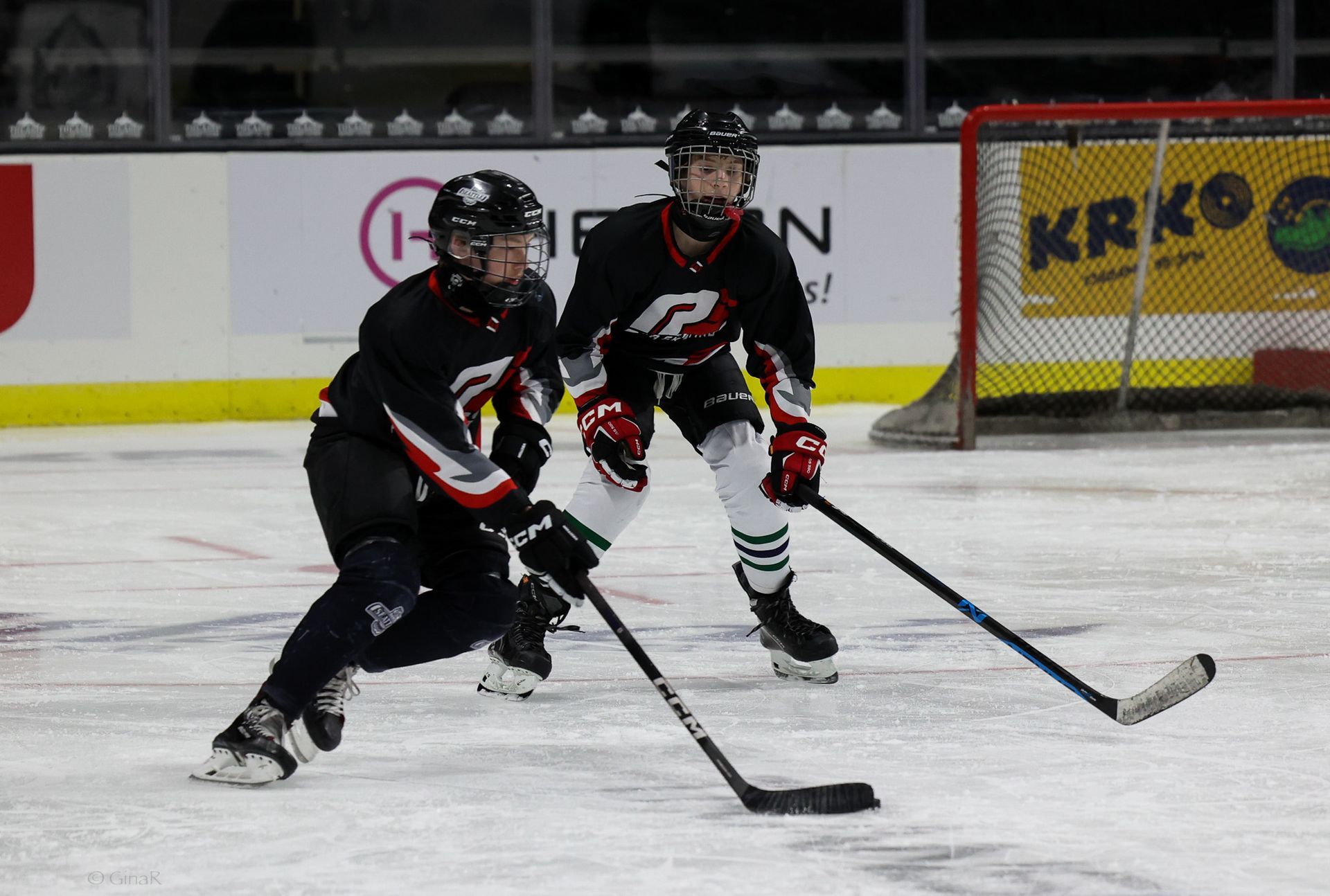 Two hockey players in black uniforms skating on ice during a game
