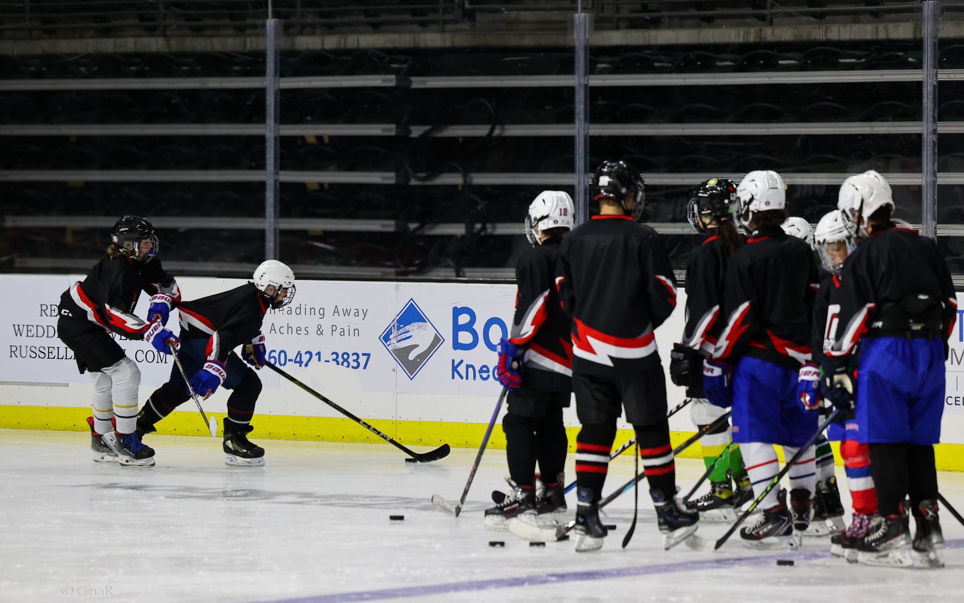 Youth ice hockey players gathered on an indoor rink during practice, with one player skating left.