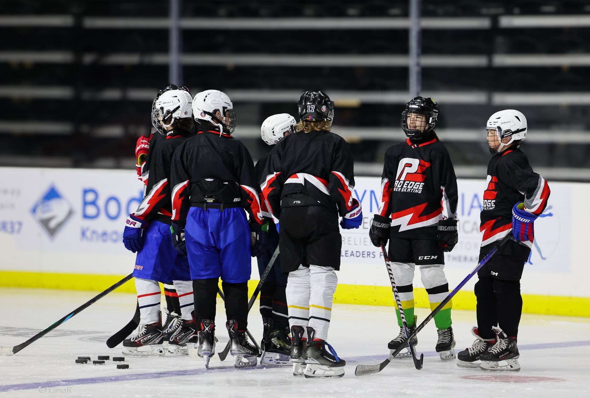 Youth hockey players huddle on the ice in black, blue, and white uniforms during a game pause