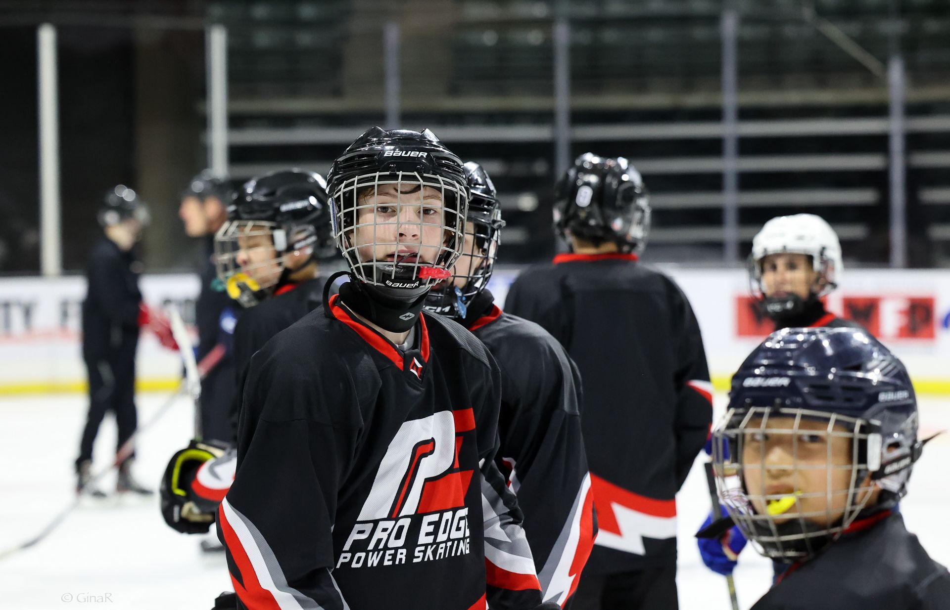 Youth hockey players in black jerseys and helmets on an indoor rink, one facing the camera.