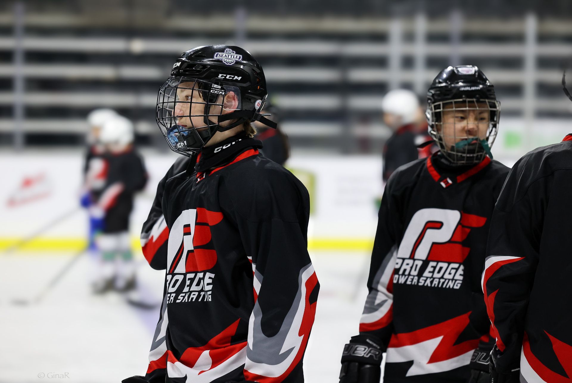 Two hockey players in black-and-red jerseys on an ice rink, wearing helmets and face cages.
