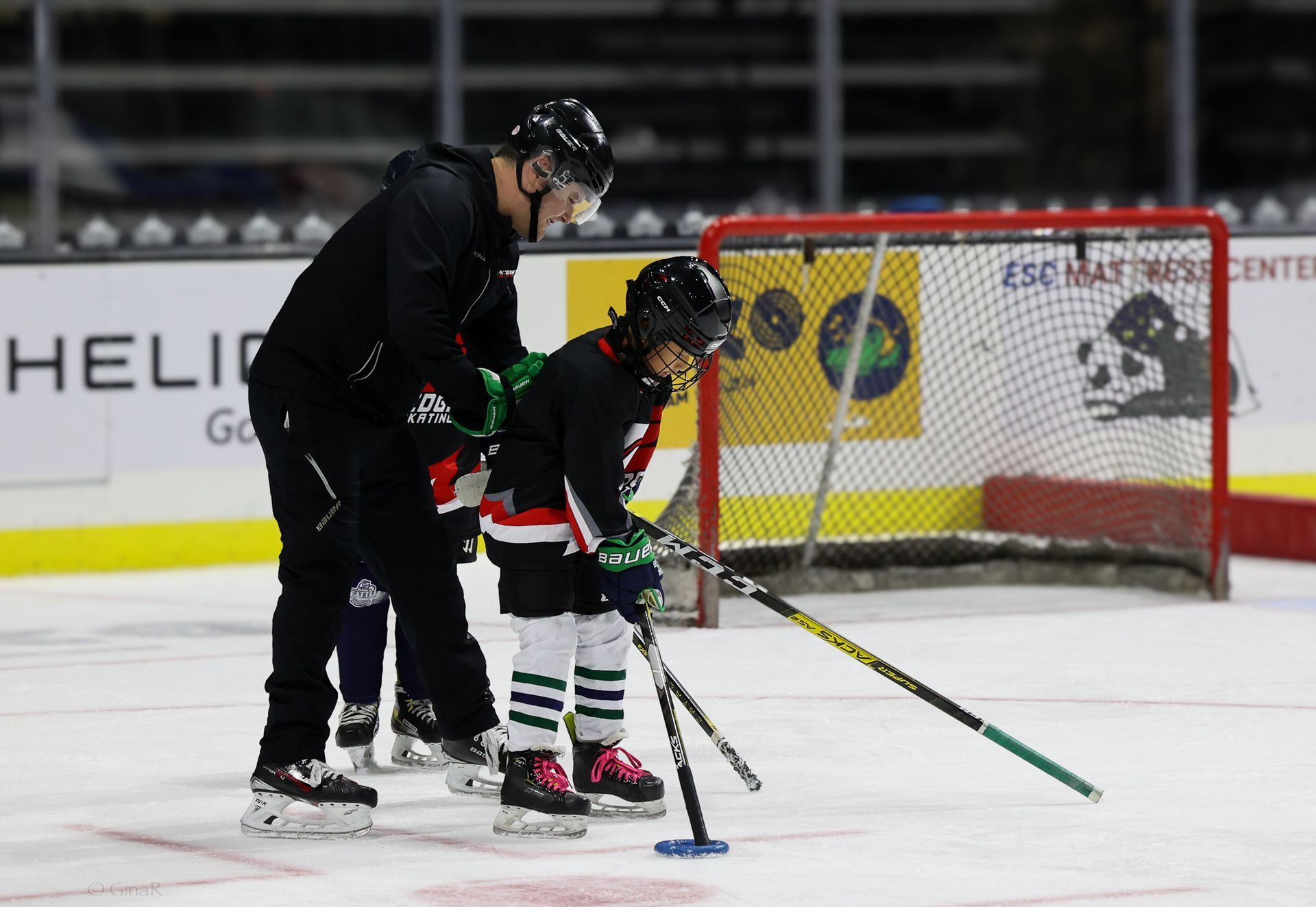 A man is teaching a young boy how to play hockey on the ice.