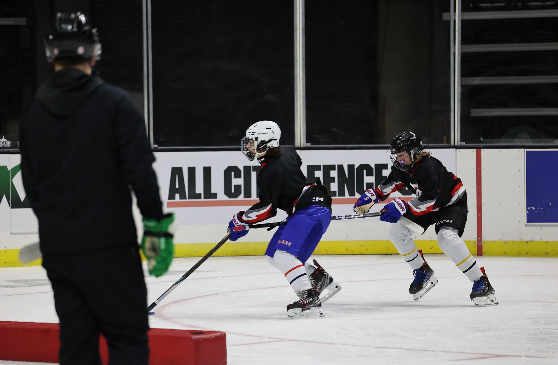Two hockey players race for the puck on an indoor ice rink, one in blue leading a defender in white and black.