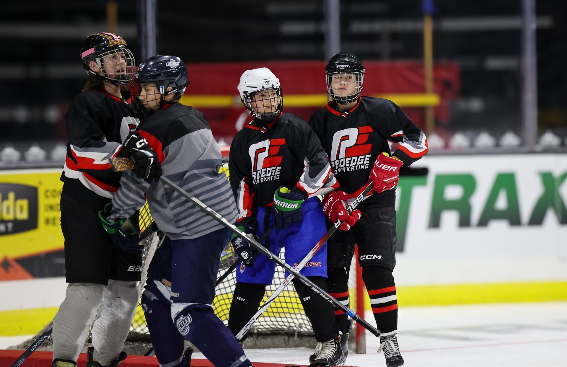 Ice hockey players in black and red gear huddle on the rink near the boards.