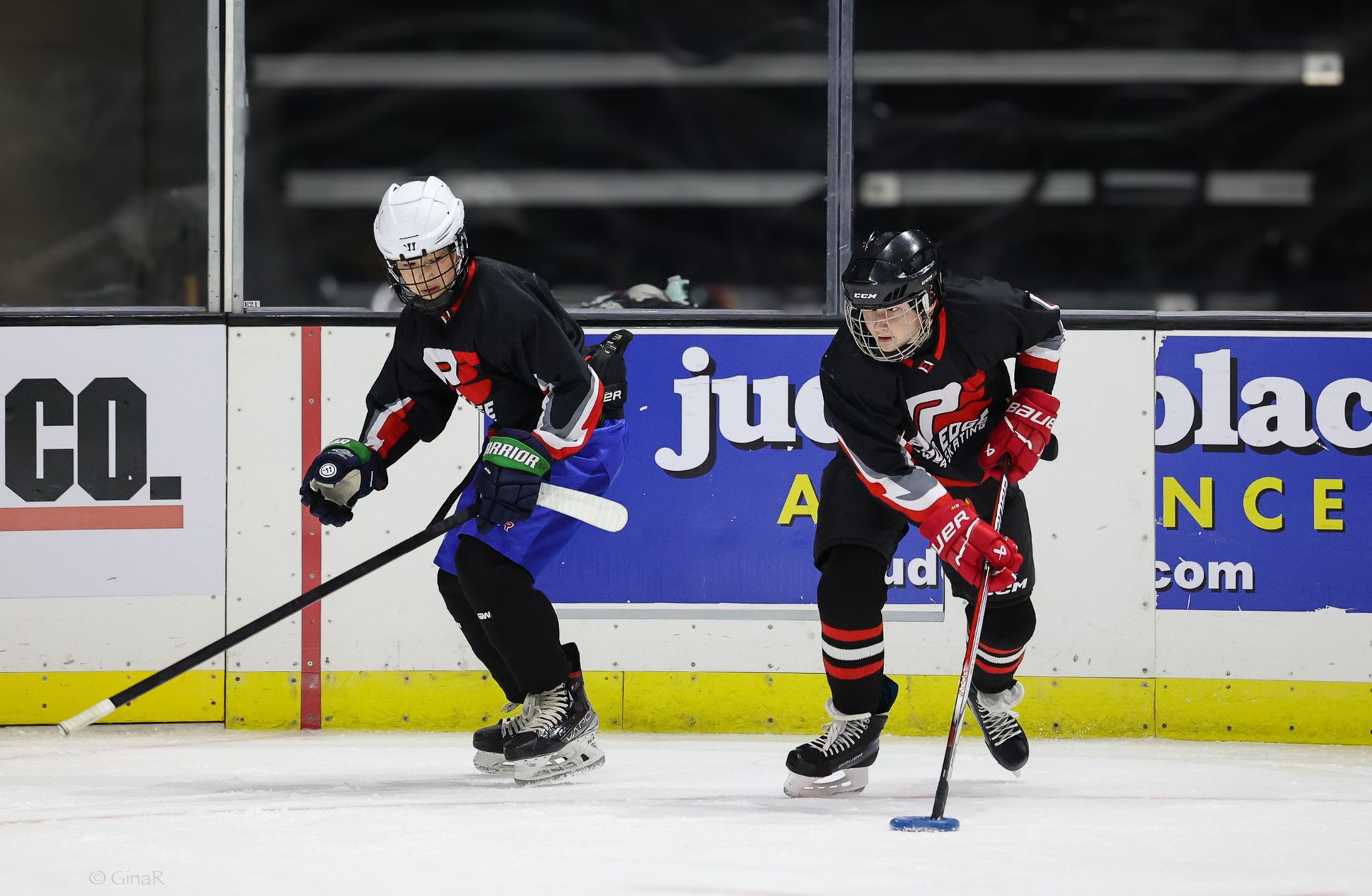 Two hockey players in black and red uniforms race after the puck on the ice.