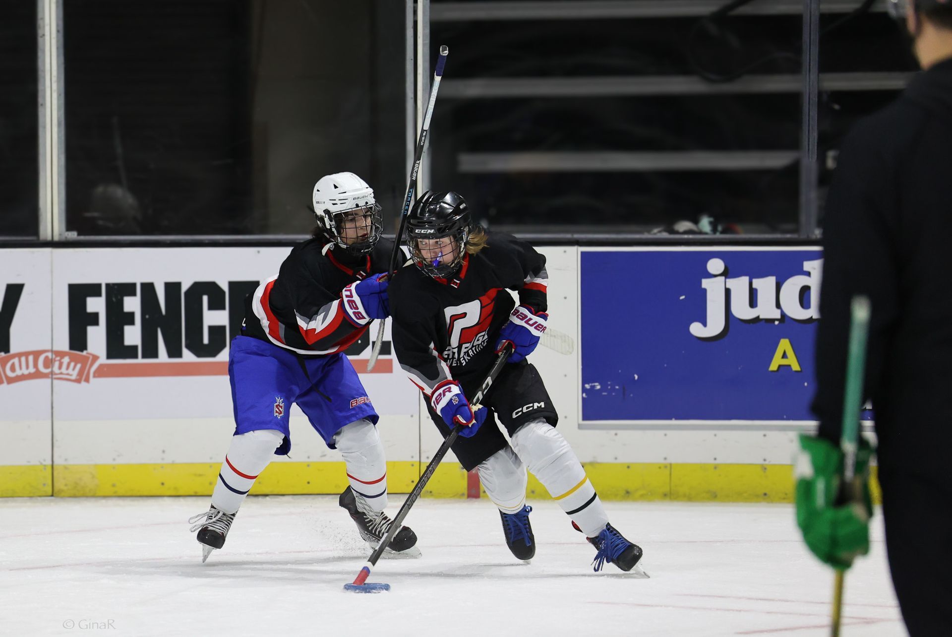 Two hockey players in black and white jerseys battle for the puck near the boards