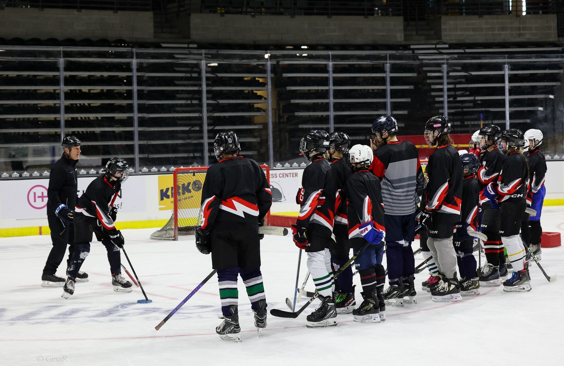 Ice hockey team huddles on the rink, wearing black jerseys and helmets during practice.