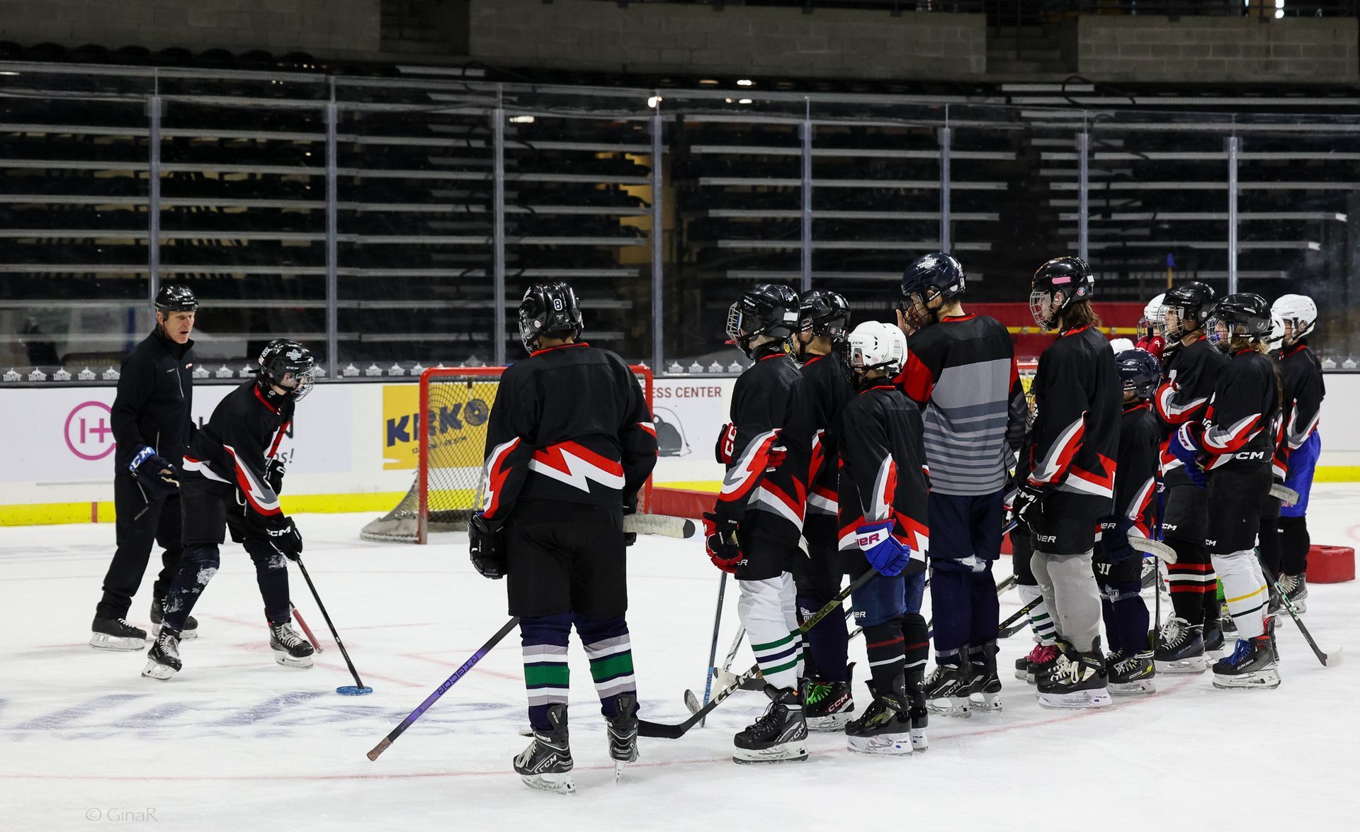 Hockey players in black jerseys gather on an indoor ice rink during a timeout.