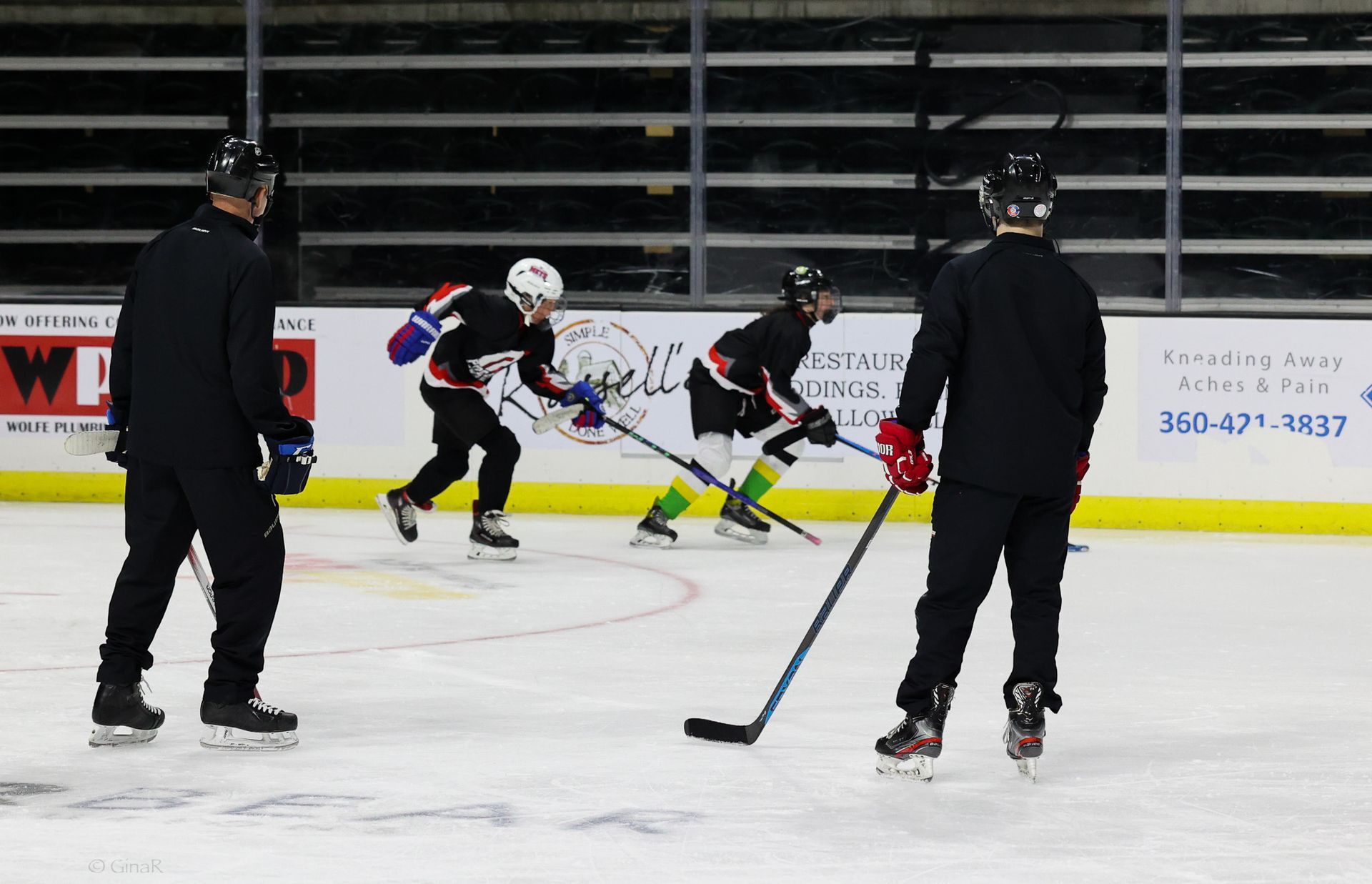Youth hockey players in black jerseys skating on an indoor ice rink during practice