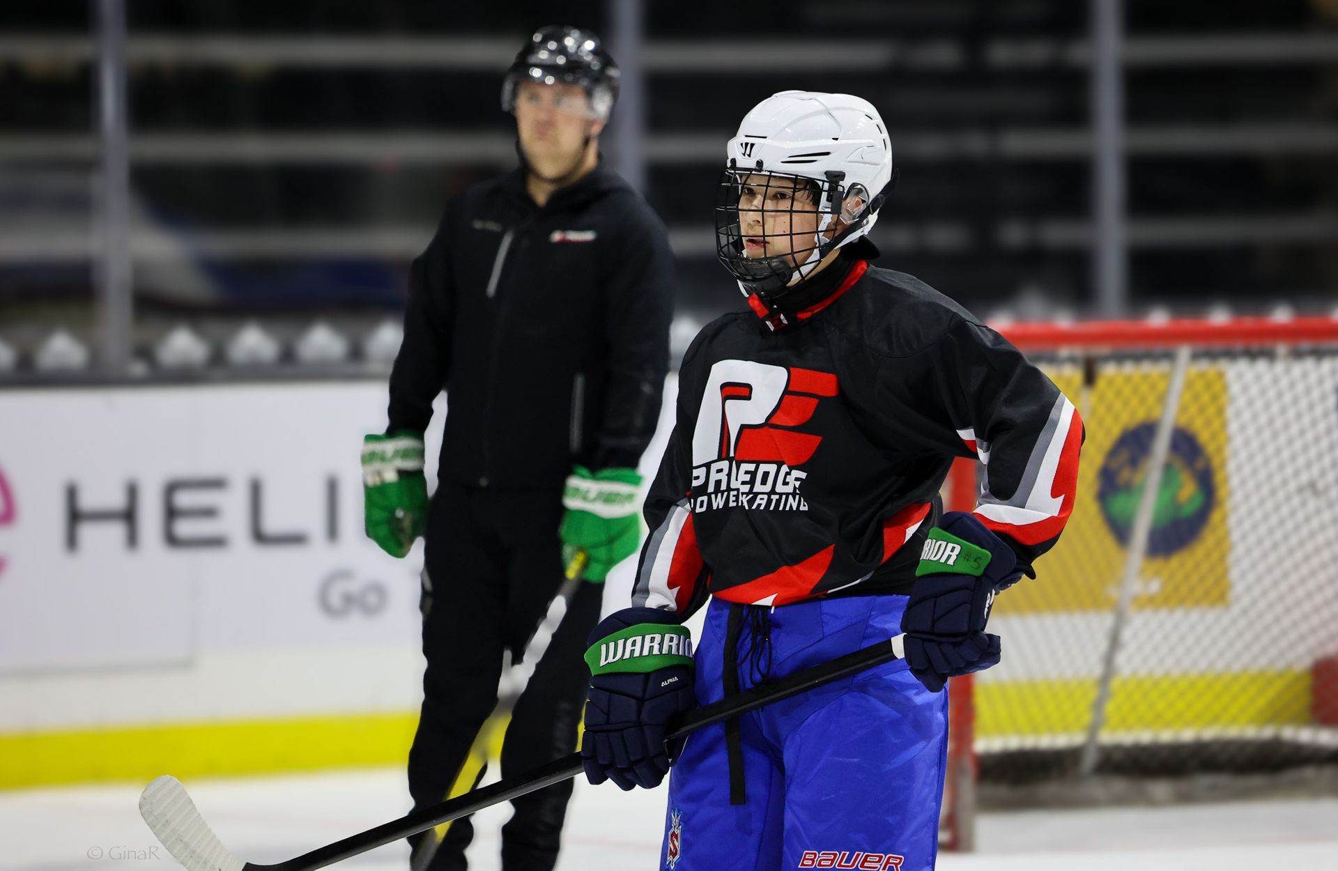 Two hockey players on an indoor rink, one in black and blue gear in the foreground.