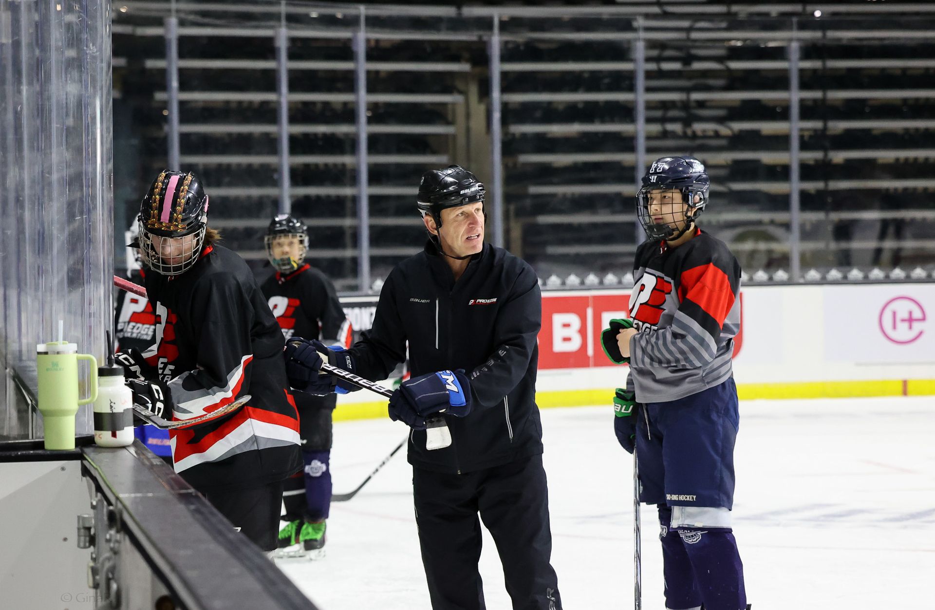 Ice hockey players and coach standing by the boards during practice on an indoor rink.