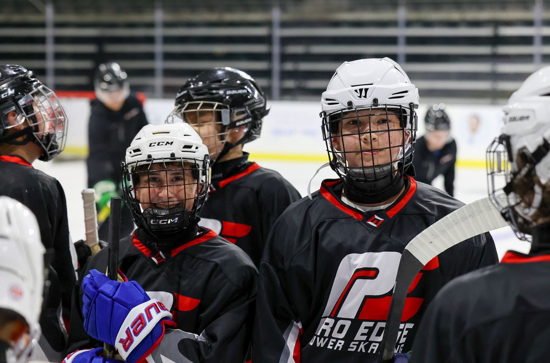 Hockey players in black and red gear line up on an indoor ice rink, facing the camera.